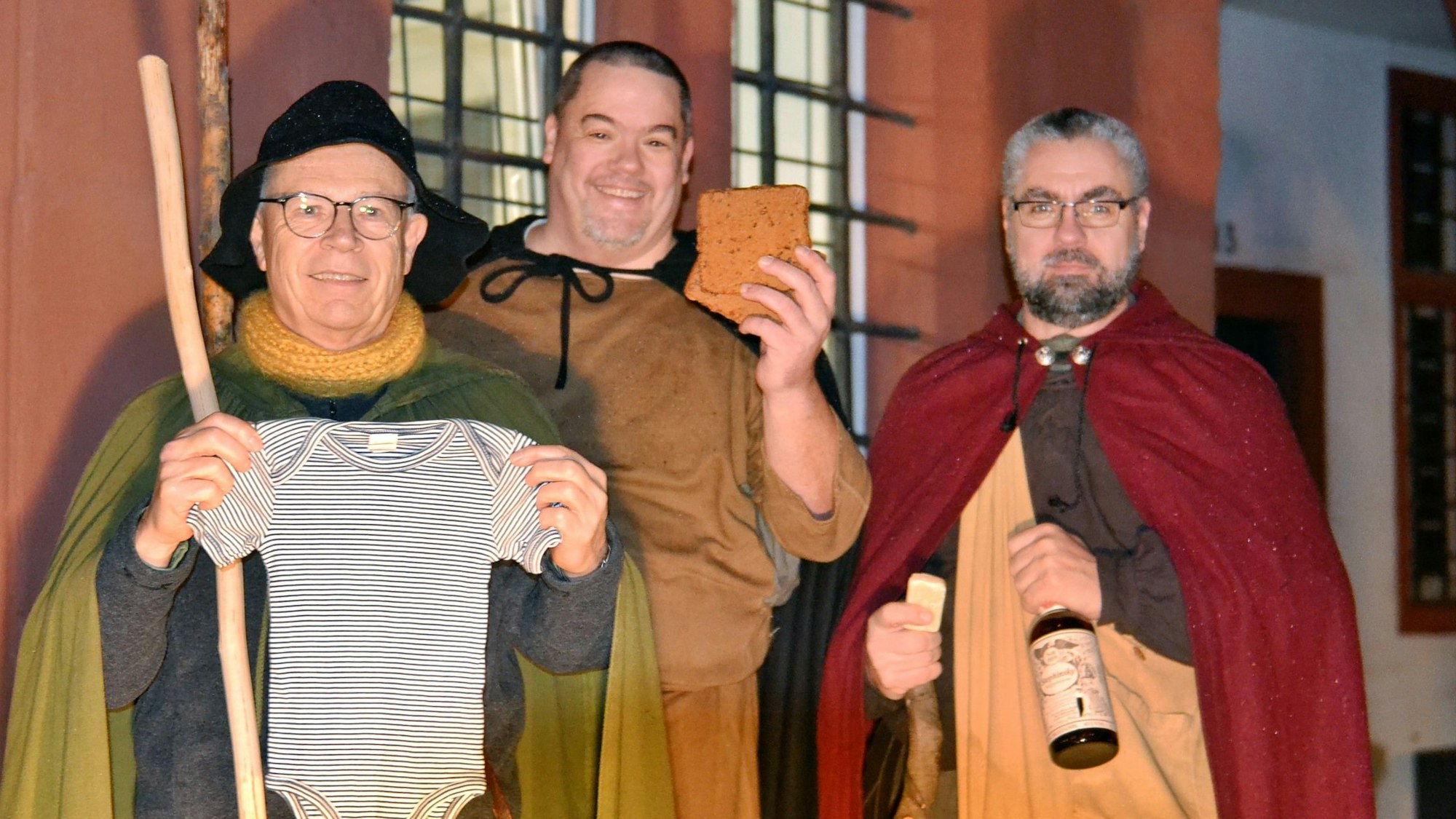 Drei verkleidete Männer haben einen Strampler, Printen und eine Flasche Likör dabei.