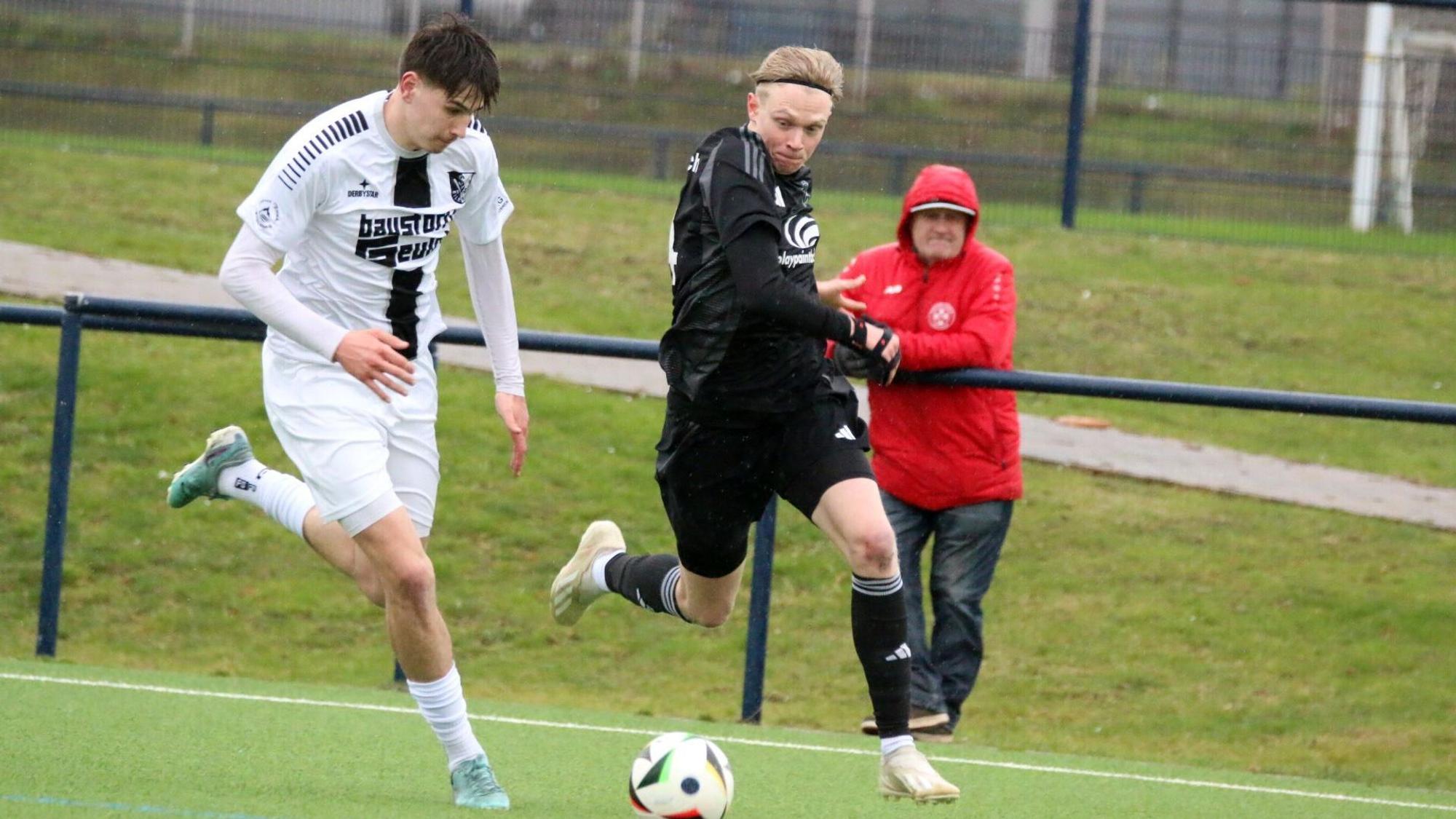 Tim Birkenheuer im Laufduell mit einem Gegenspieler. Im Hintergrund steht ein Zuschauer, der die Kapuze über den Kopf gezogen hat.