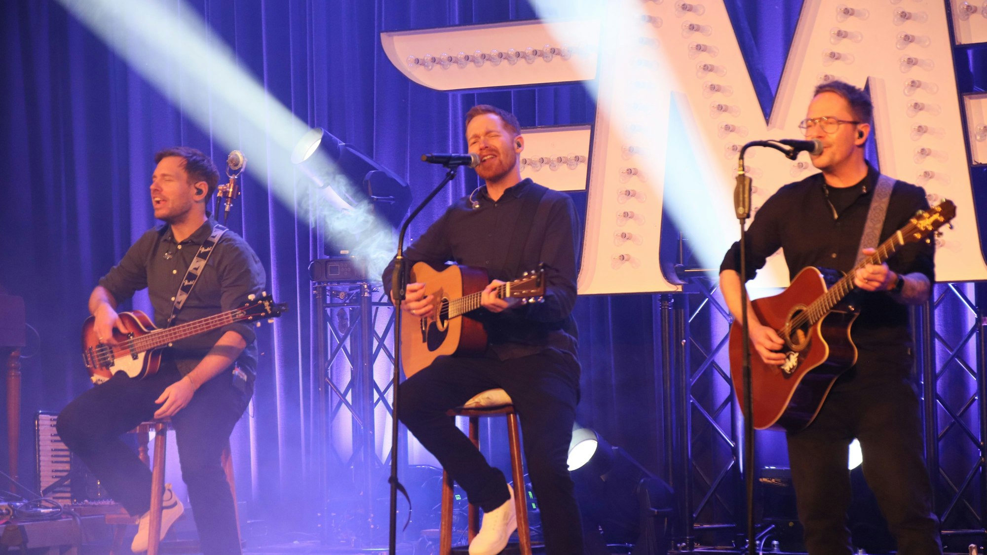 Drei Musiker mit Gitarren auf einer Bühne.