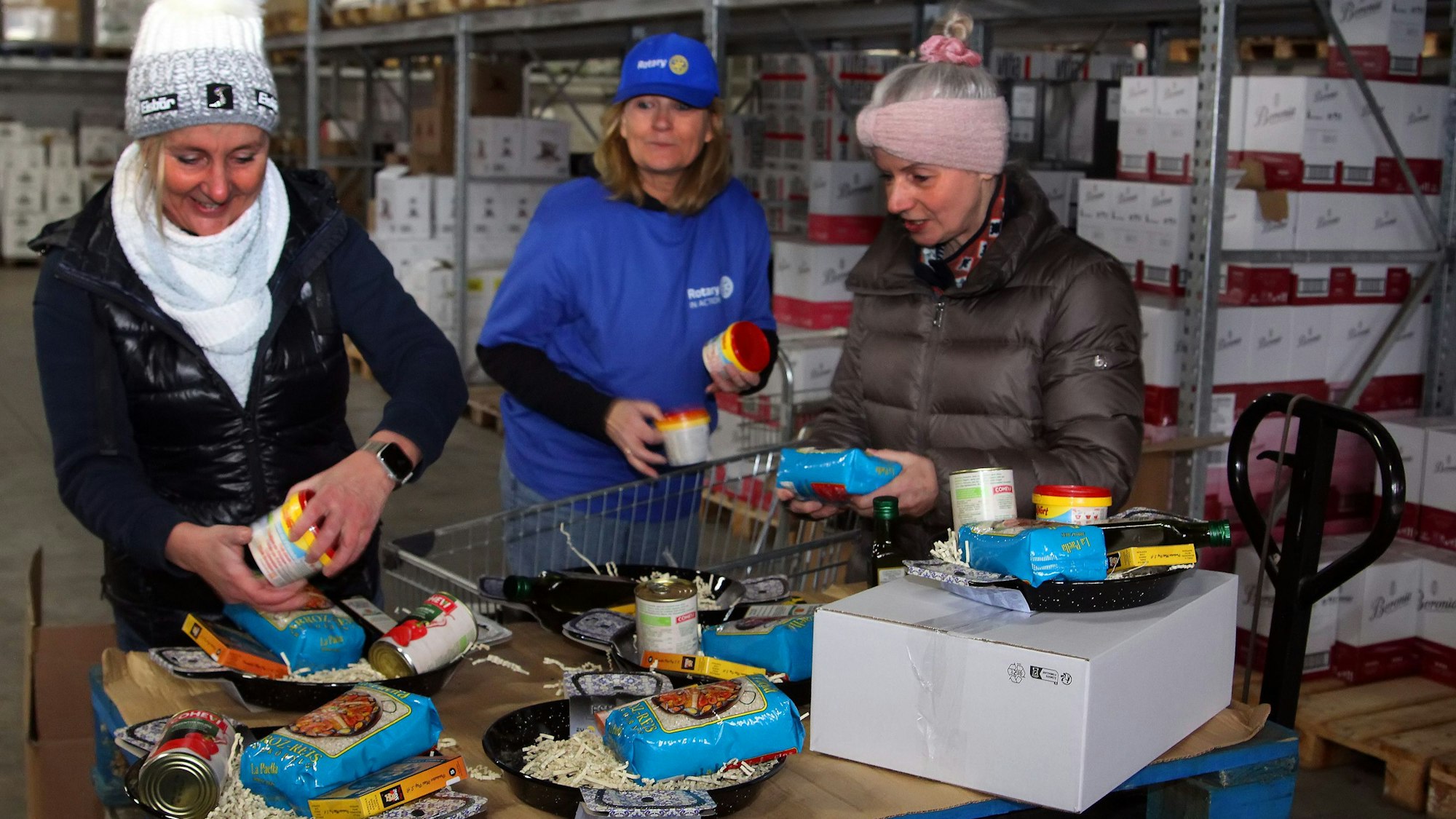 Auf dem Foto sind drei Frauen in einem Lager zu sehen, die Geschenkboxen zusammen stellen.
