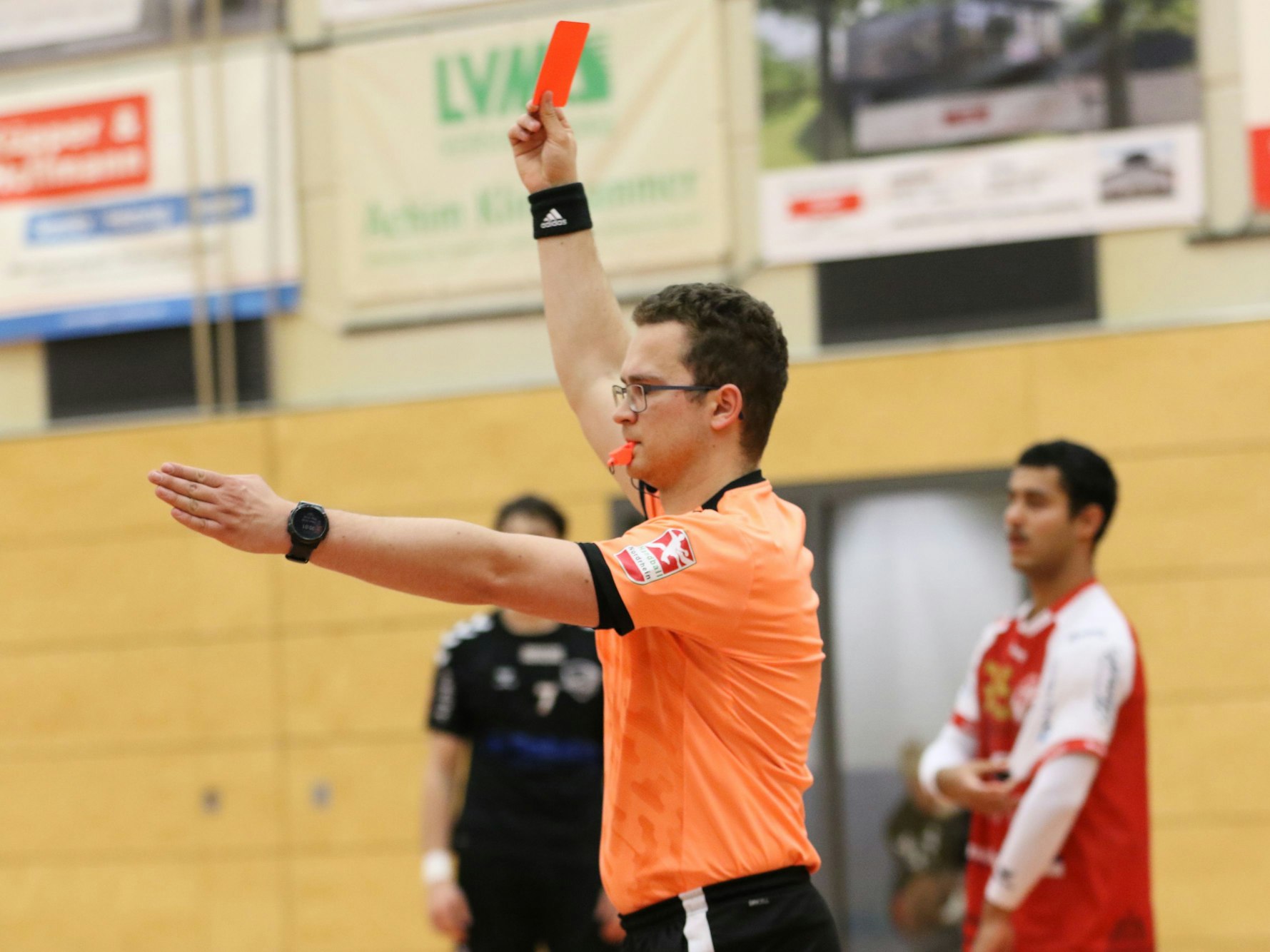 Ein Schiedsrichter zeigt die Rote Karte und streckt den linken Arm nach vorne.
