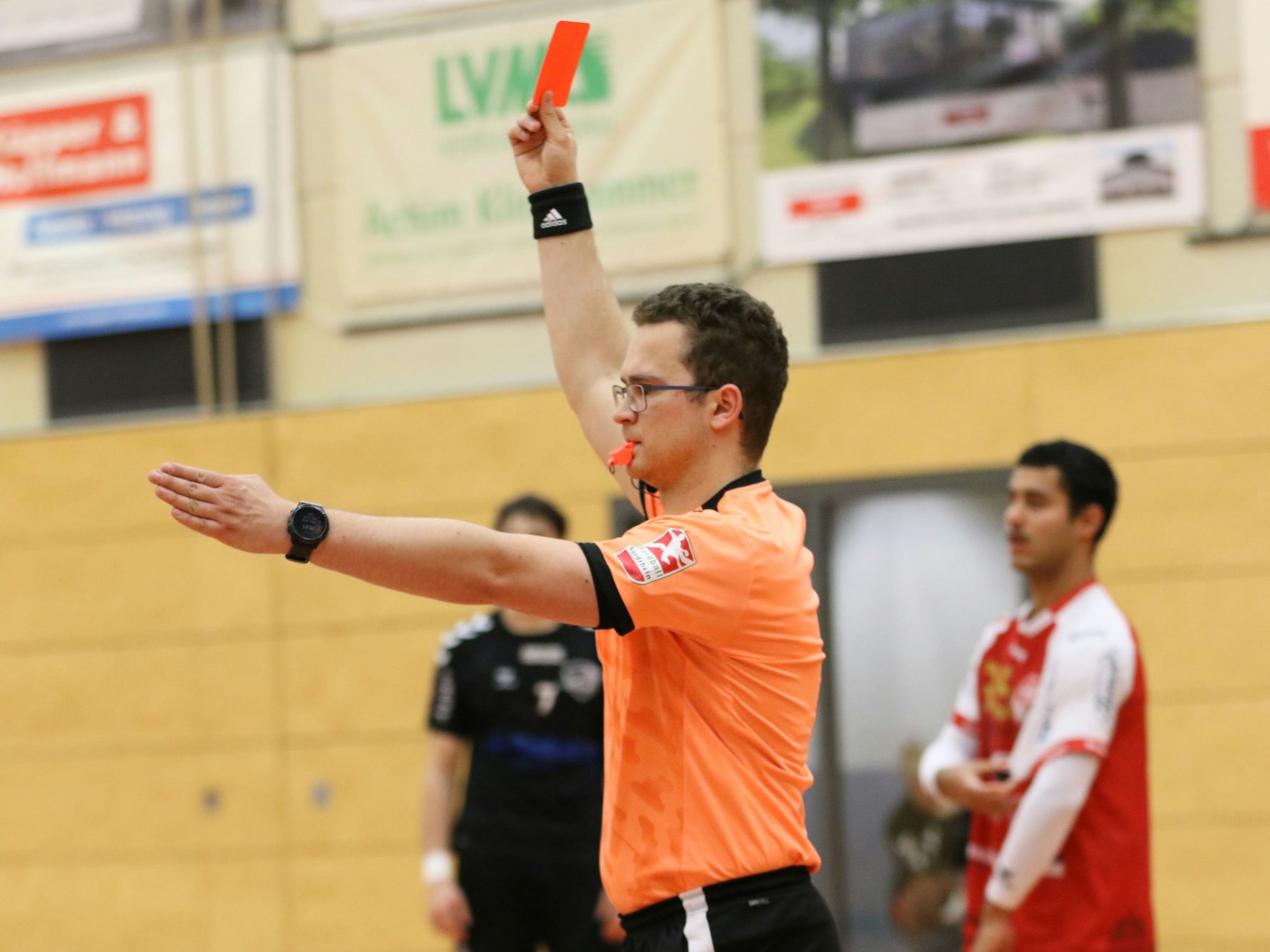 Ein Schiedsrichter zeigt die Rote Karte und streckt den linken Arm nach vorne.