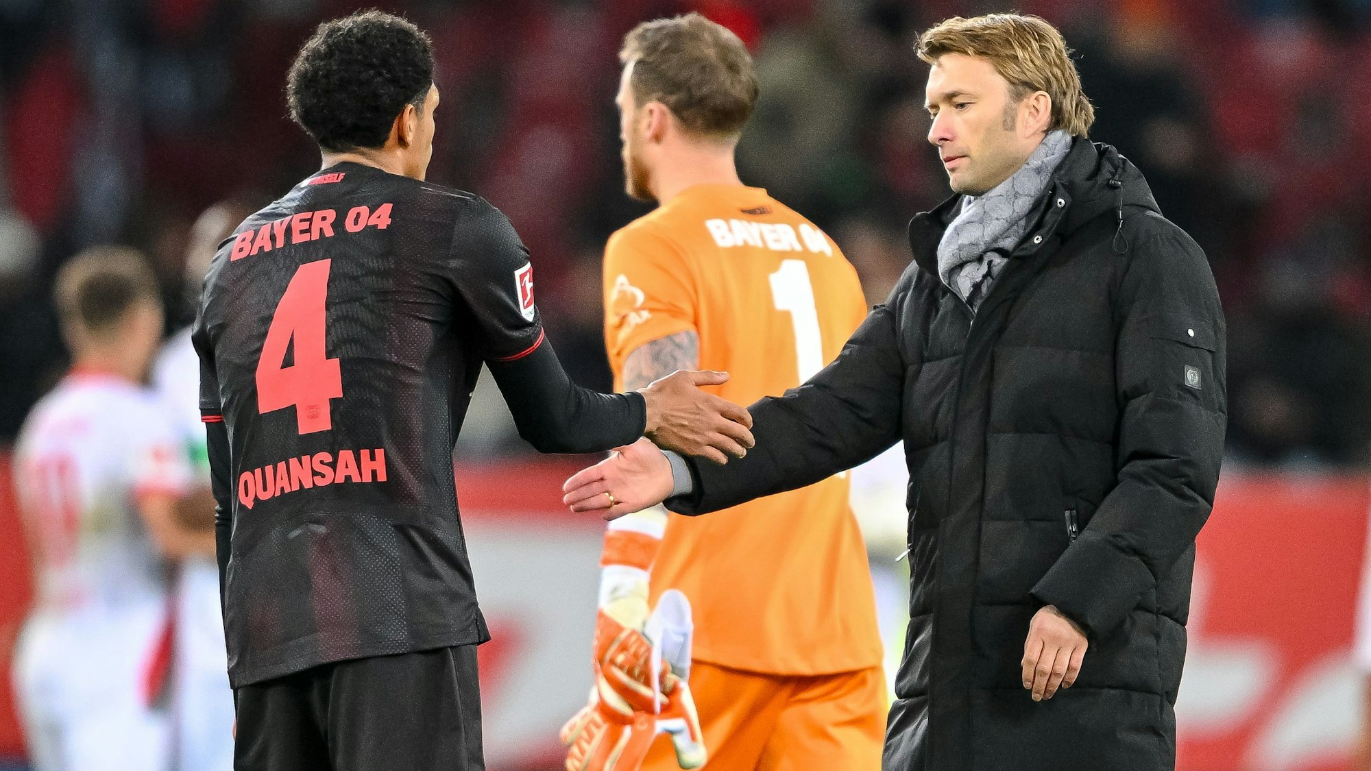 Jarell Quansah (l, Bayer Leverkusen), Torwart Mark Flekken (Bayer Leverkusen) und Geschäftsführer Sport Simon Rolfes (Bayer Leverkusen) klatschen sich nach dem 0:2 in Augsburg enttäuscht ab.