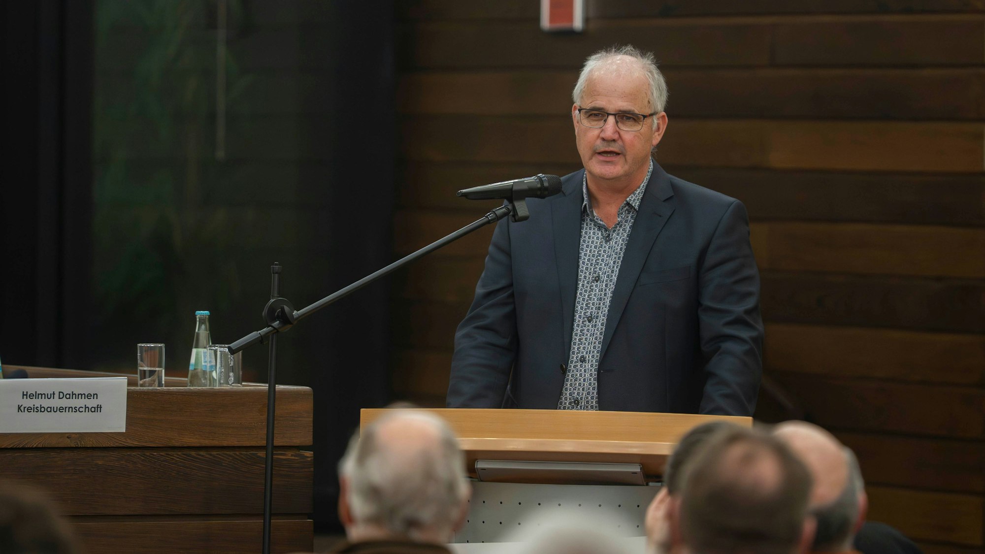 Helmut Dahmen,steht am Mikrofon, vor ihm sieht man von hinten Menschen im Publikum.