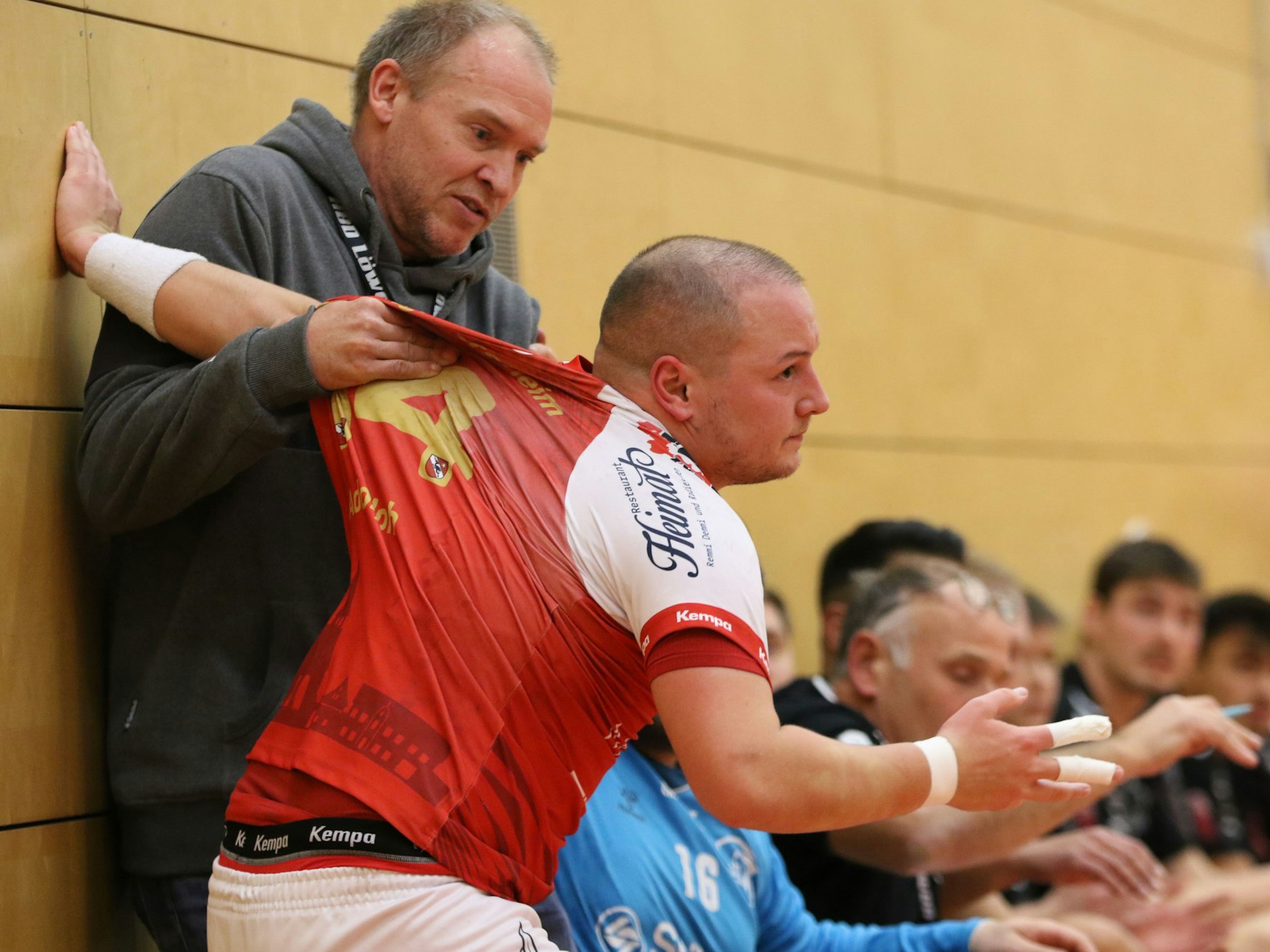 Der Trainer von Oberberg packt Niklas Adolph am Trikot. Der stützt sich mit einer Hand an der Wand ab. Was bedrohlich aussieht, war eine Rettungsaktion des Trainers, weil Adolph ist die Gästebank zu stürzen drohte.