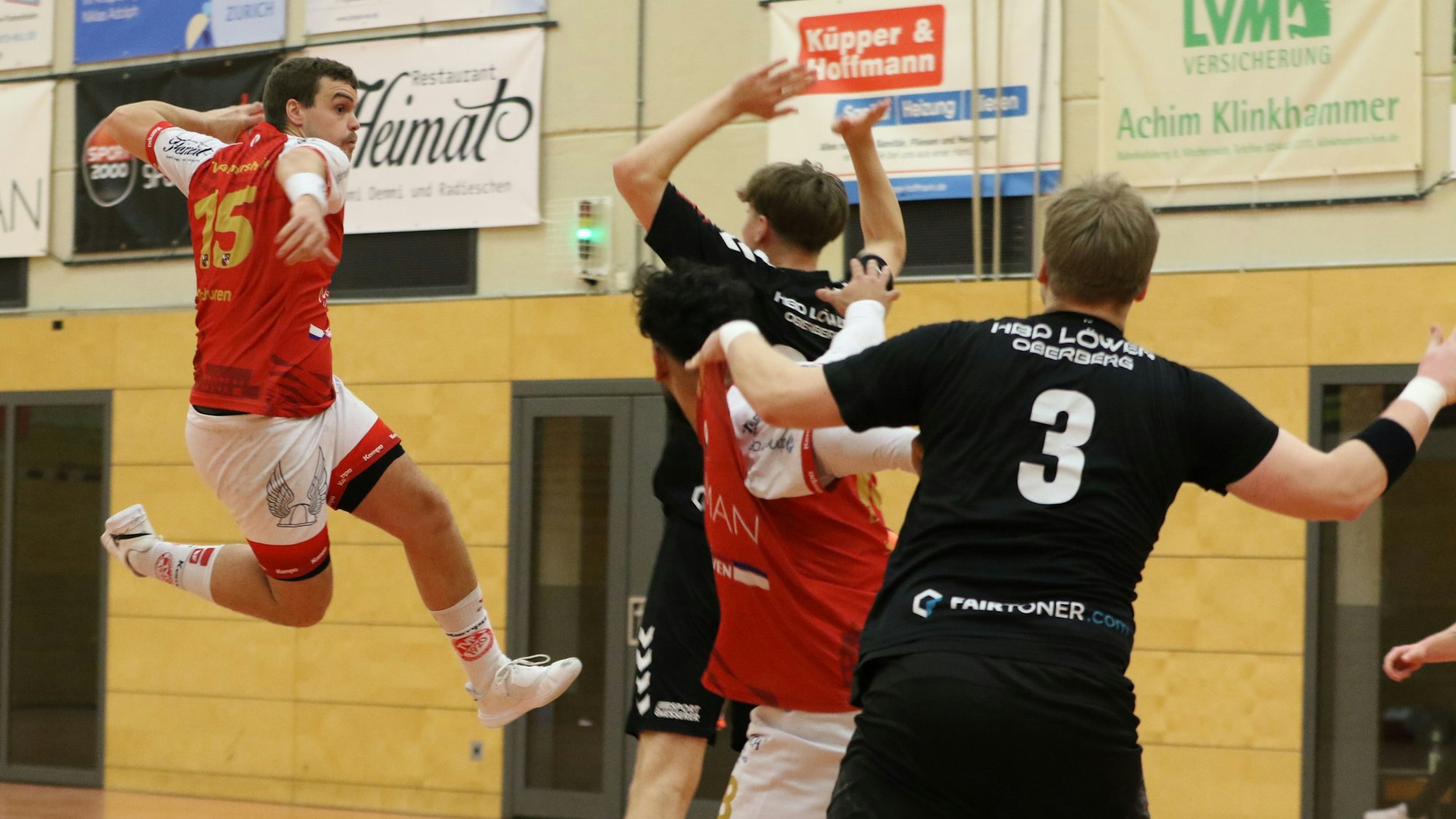 Palmersheims Spieler Nils Schouren steigt zum Wurf hoch. Ein Gegner vor ihm reißt die Arme hoch. Hinter ihm befinden sich ein Mitspieler und ein weiterer Gegenspieler.