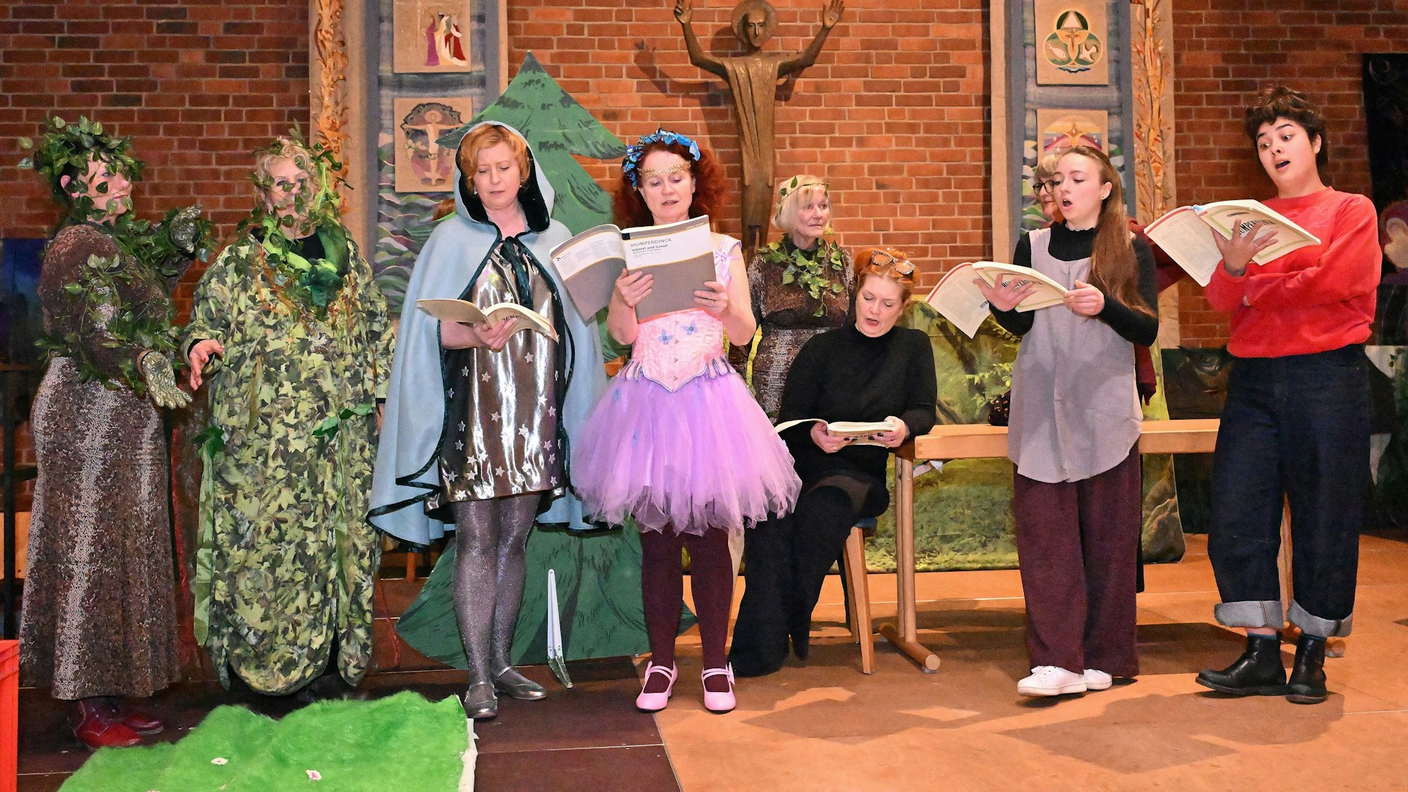 Auf einer Bühne stehen als Waldfiguren verkleidete Menschen und proben mit einem Textbuch in der Hand.