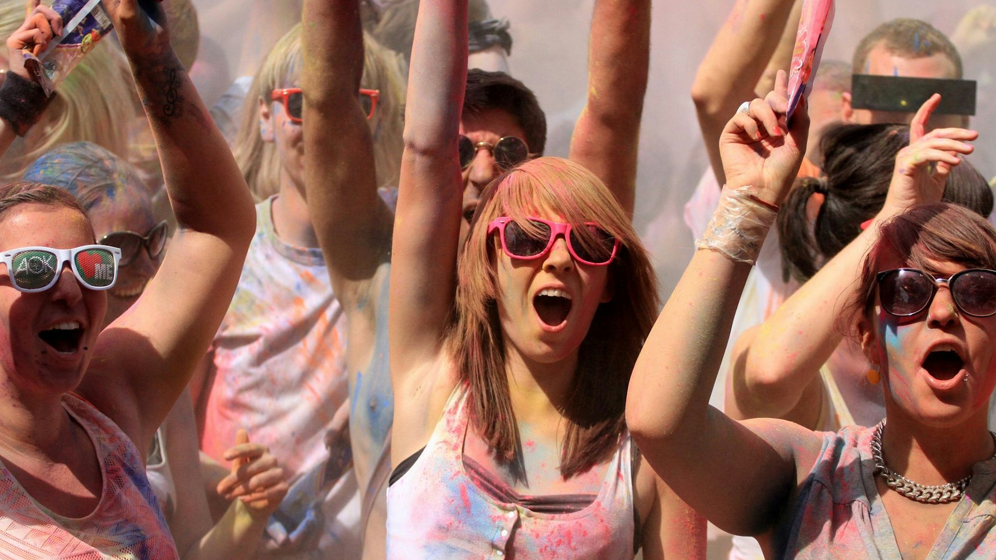 Junge Menschen, mit Pulverfarbe beschmiert, recken die Hände in die Höhe und singen zu Musik mit.