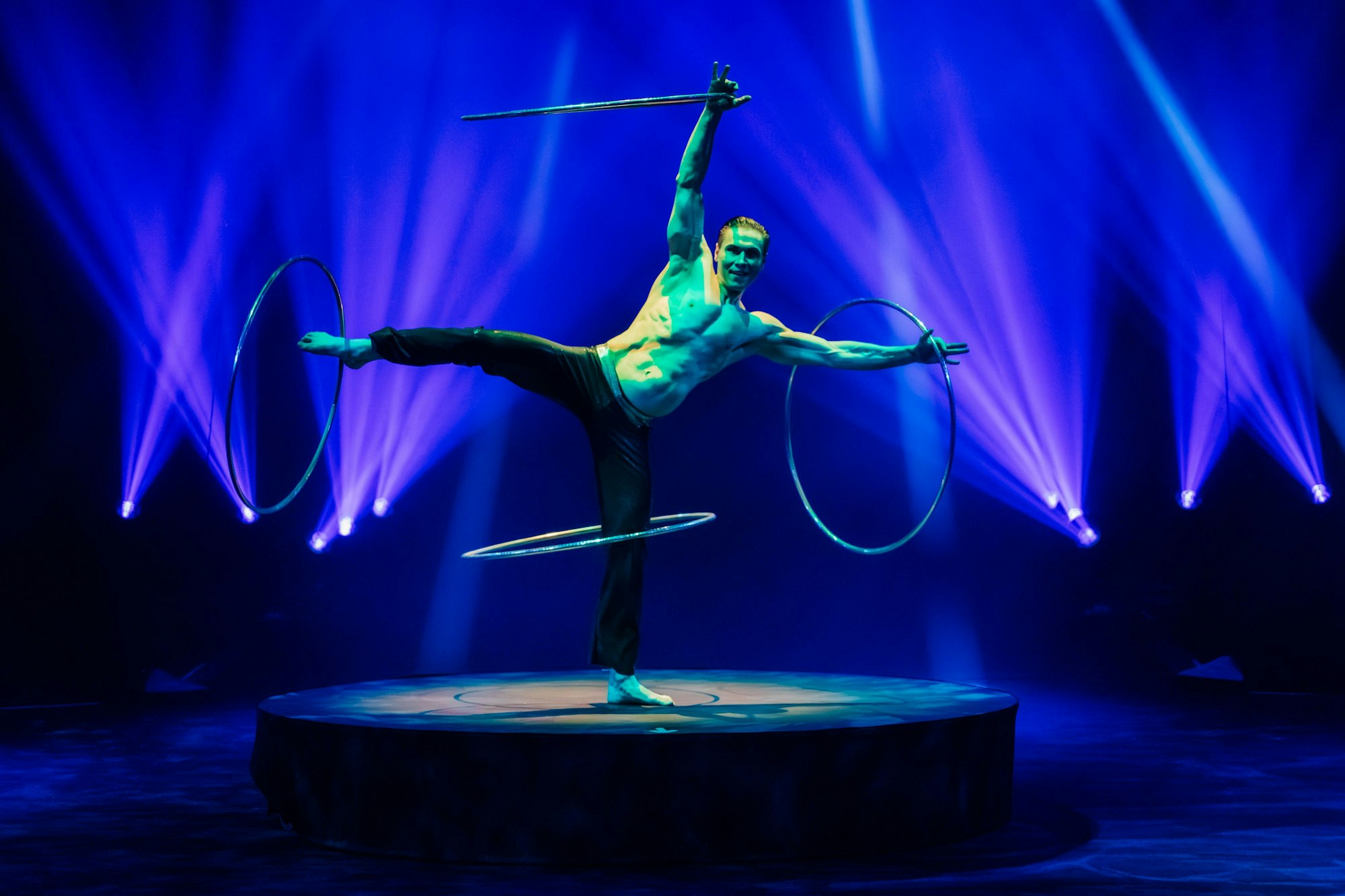 Das Bild zeigt einen Artisten im Zirkus, der 4 Reifen an seinen Armen uns Beinen schwingt.