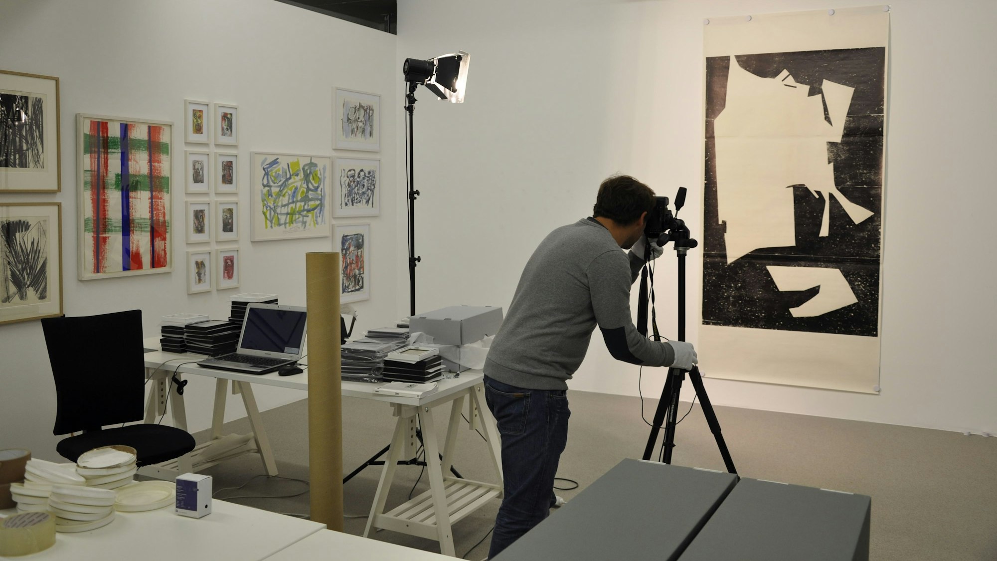 Ein Mann fotografiert ein Kunstwerk, es hängt an einer Wand.