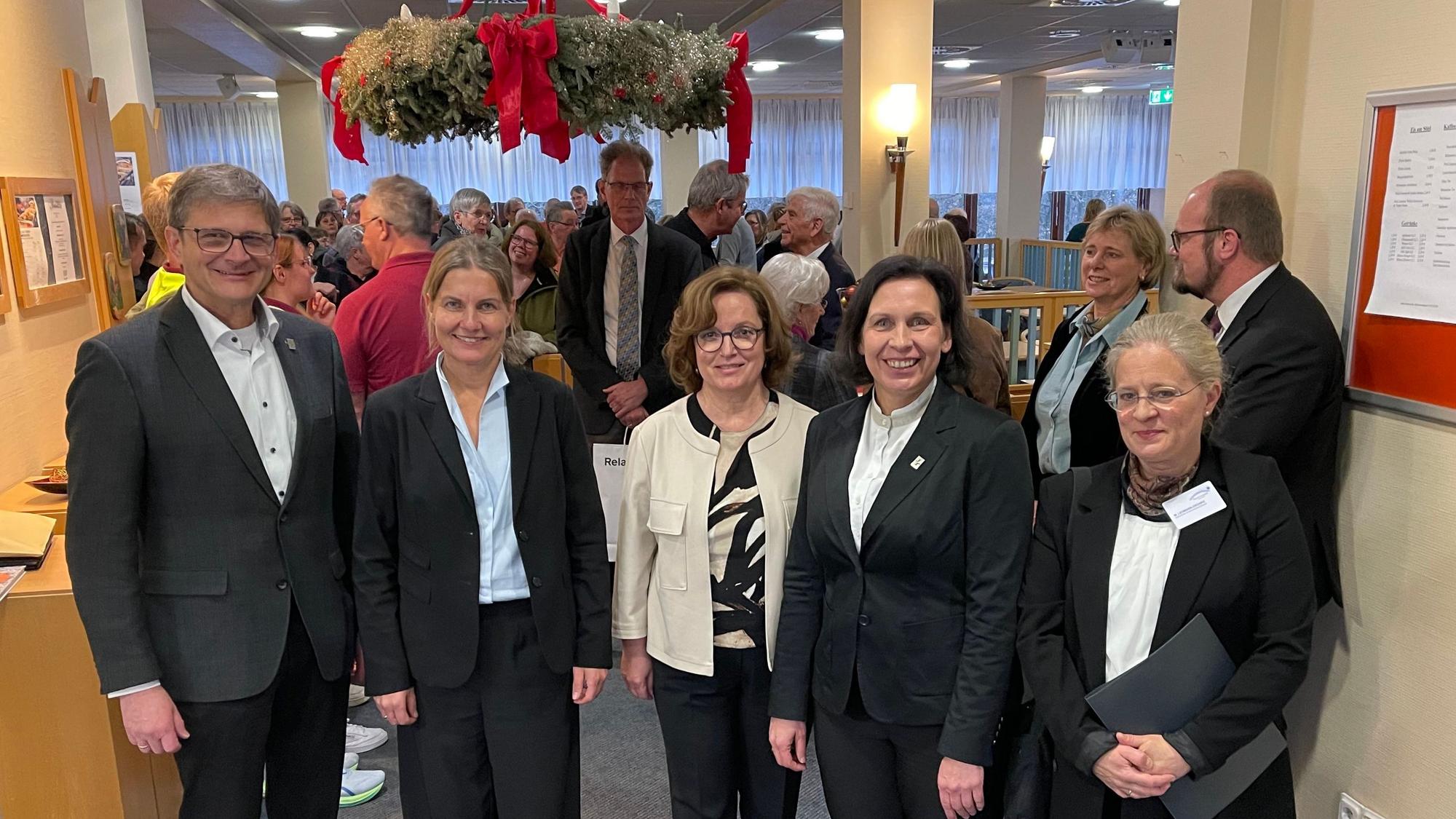 Der Mann und die vier Frauen stehen in einer Reihe am Eingang der Cafeteria, in der sich weitere Gäste versammelt haben.