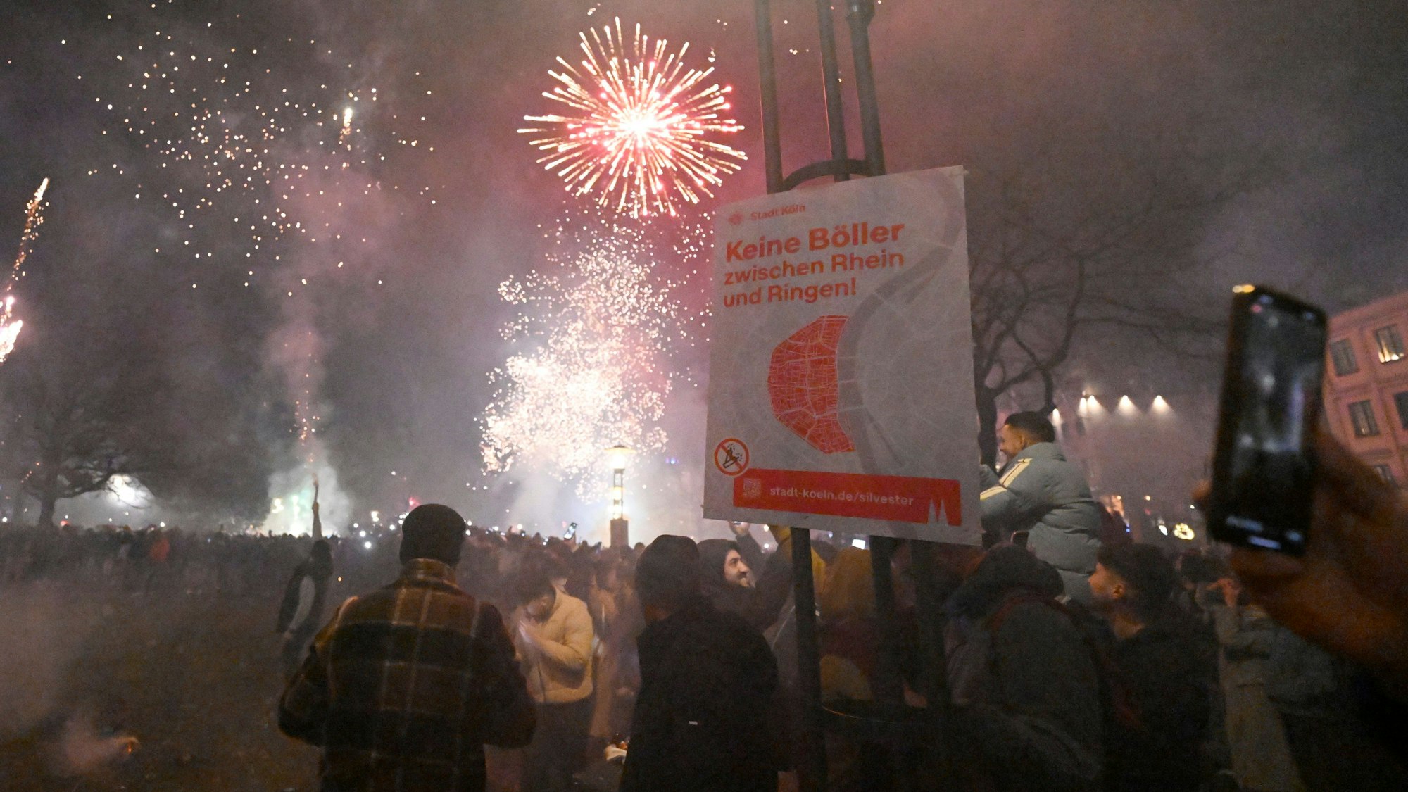 Menschen zünden in der Altstadt Feuerwerkskörper vor dem Böllerverbotsplakat um das neue Jahr 2024 willkommen zu heissen.