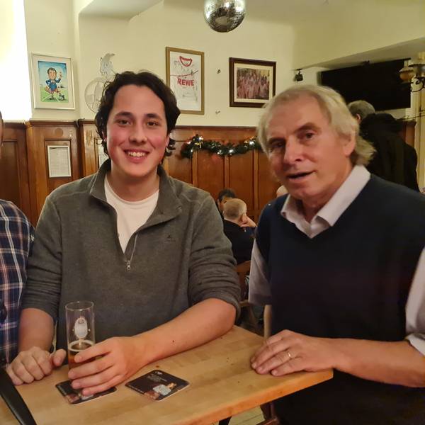 Drei Männer stehen an eine Theke, vor dem Mann ganz links steht ein Aufnahmegerät auf der Theke.