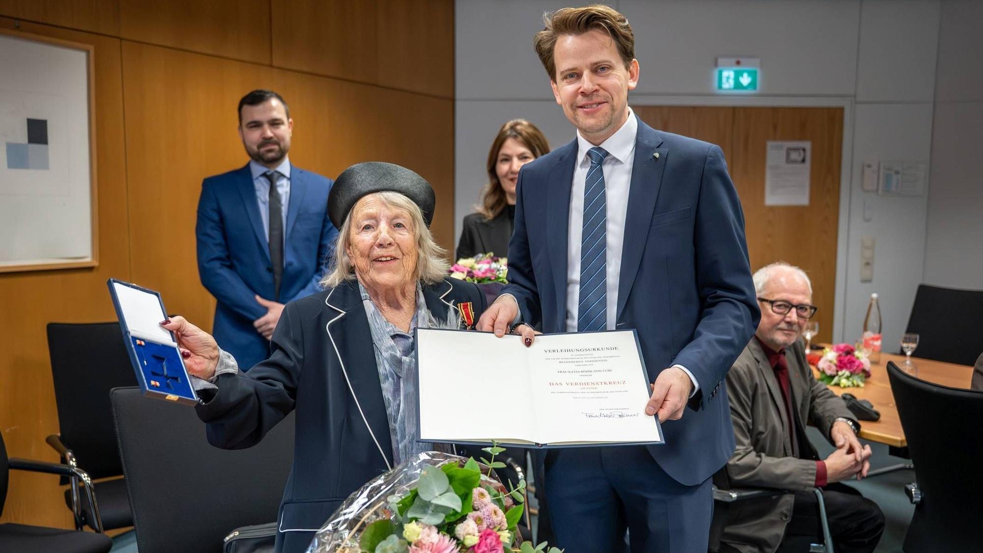 Eine ältere Dame und ein jüngerer Mann schauen in die Kamera und lächeln.