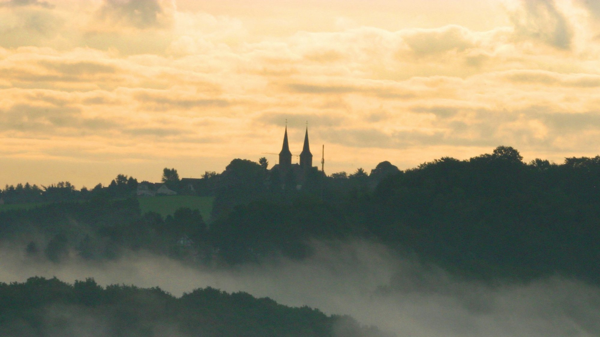 Die Kirche St. Maria Heimsuchung ist über den Nebelschwaden in Overath zu sehen.