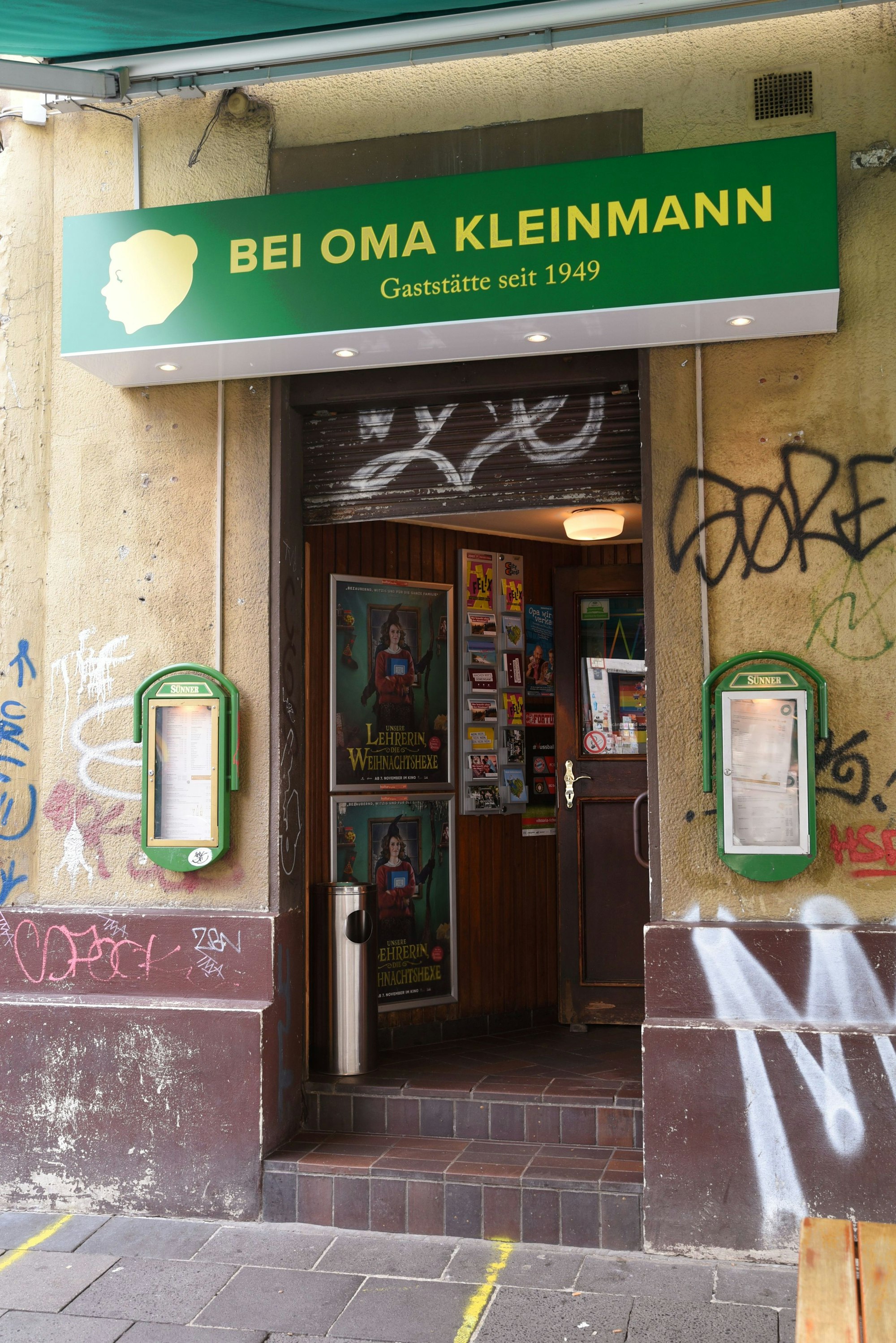 Die Eingangstür zu einer Kneipe ist zu sehen, über der Tür steht der Name „Bei Oma Kleinmann“.