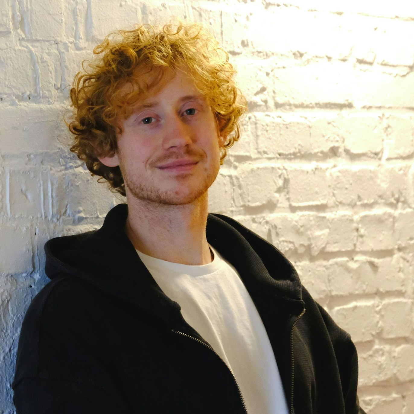 Der Comedian Vincent Tophoven lehnt an einer weiß gestrichenen Ziegelwand.