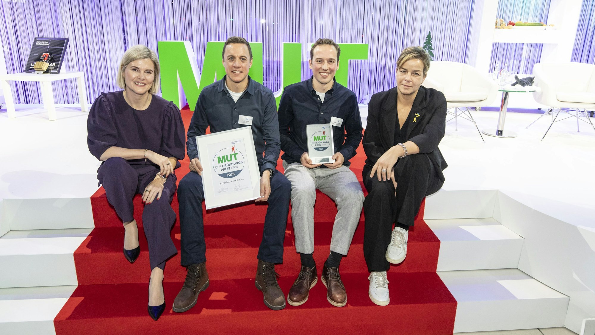 Das Foto zeigt die Preisträger auf einer Treppe mit rotem Teppich sitzend mit den Urkunden in der Hand.