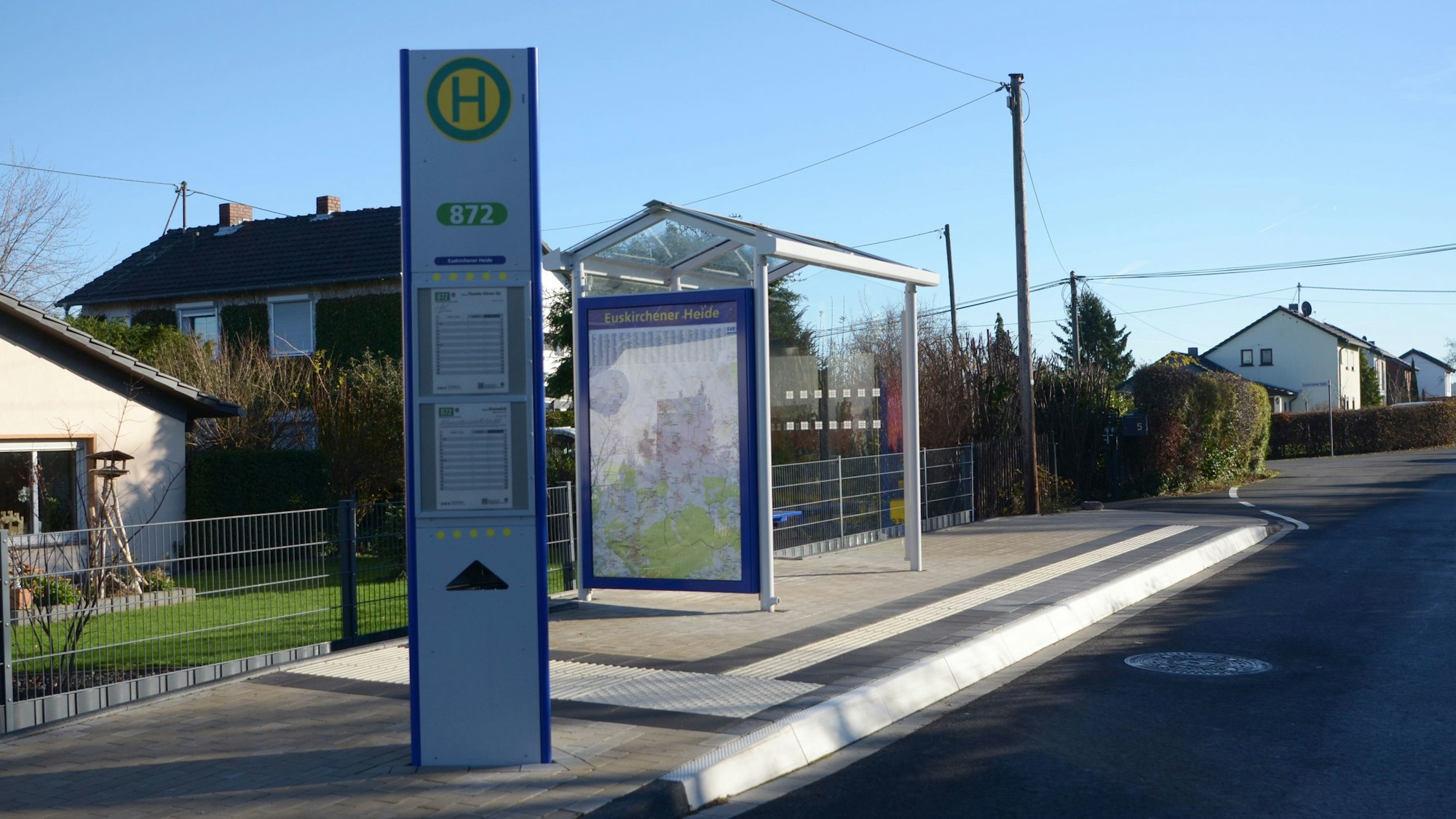 Im Vordergrund steht eine Infosäule, dahinter ein Wartehäuschen.