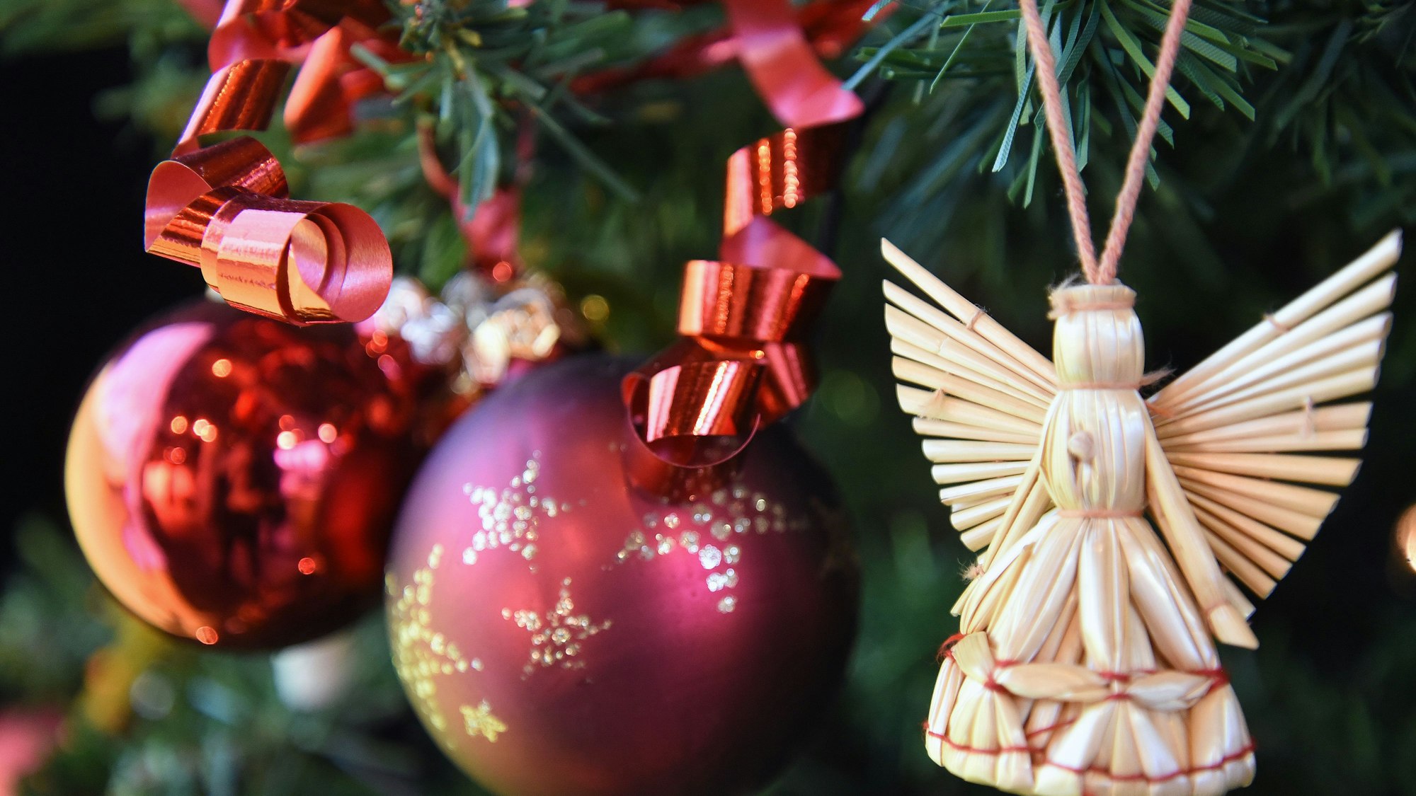 Ein Engel und zwei Weihnachtskugeln hängen in einem Baum.