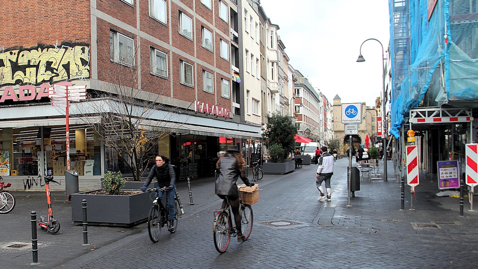 Am Eigelstein sind Radfahrer und Fußgänger unterwegs. Ein Verkehrsschild weist den Straßenabschnitt als Fahrradstraße aus.