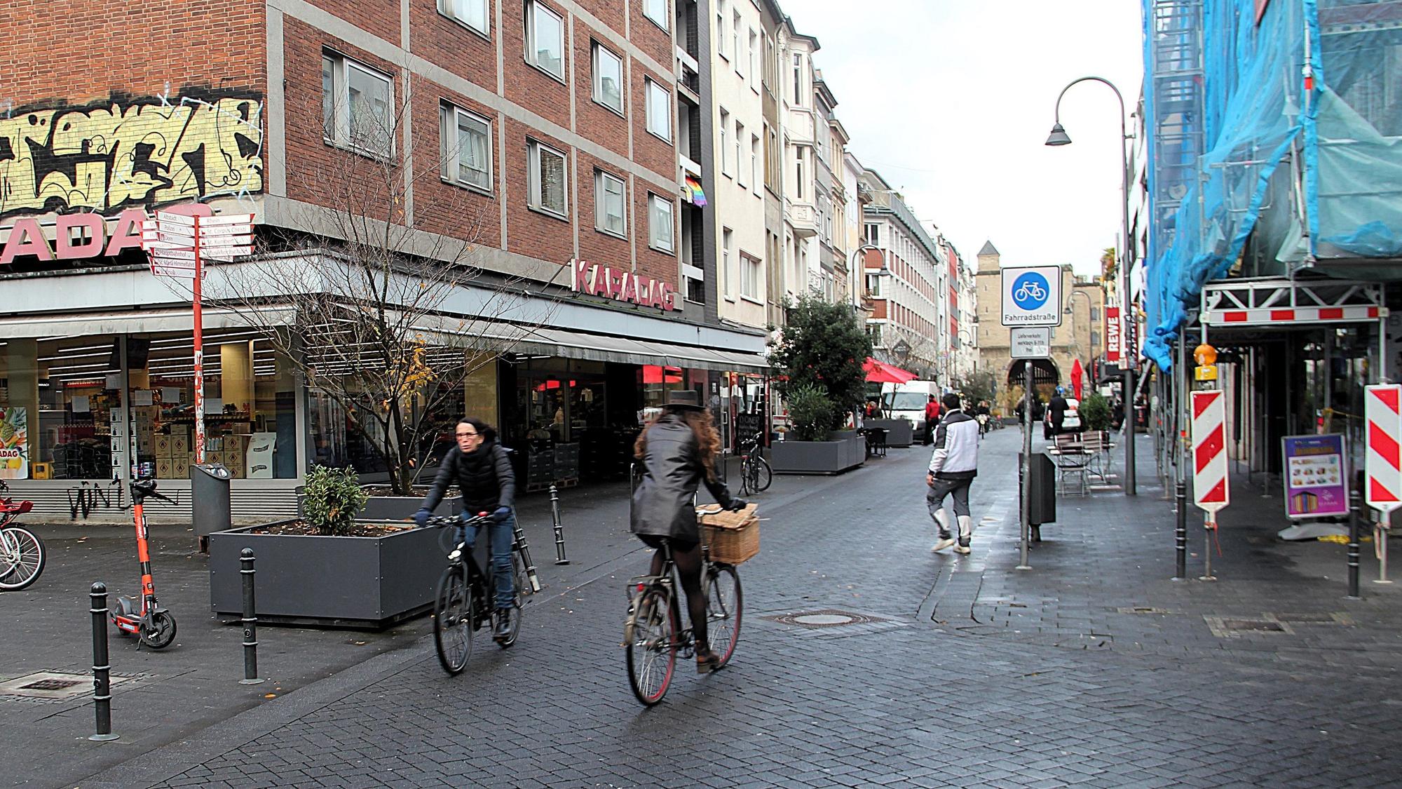 Am Eigelstein sind Radfahrer und Fußgänger unterwegs. Ein Verkehrsschild weist den Straßenabschnitt als Fahrradstraße aus.