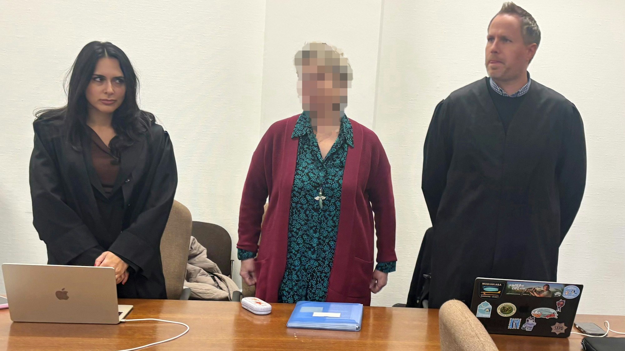 Frau steht vor Gericht, rechts von ihr eine Anwältin, links ein Anwalt.