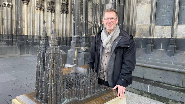 Ein Mann steht auf dem Vierungsturm des Kölner Doms, hinter ihm ragen die beiden Domtürme in den Himmel.
