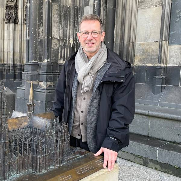 Ein Mann steht auf dem Vierungsturm des Kölner Doms, hinter ihm ragen die beiden Domtürme in den Himmel.