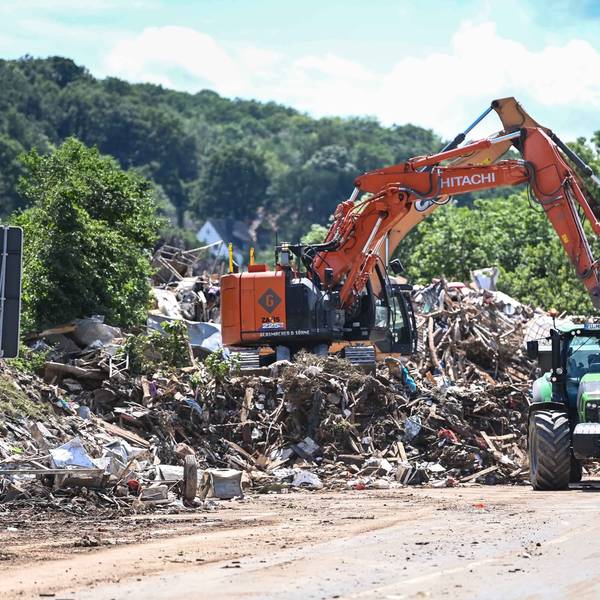 Das Bild zeigt einen Bagger, der Müll auf einen Lkw lädt. Auch ein Traktor samt Anhänger ist zu sehen.
