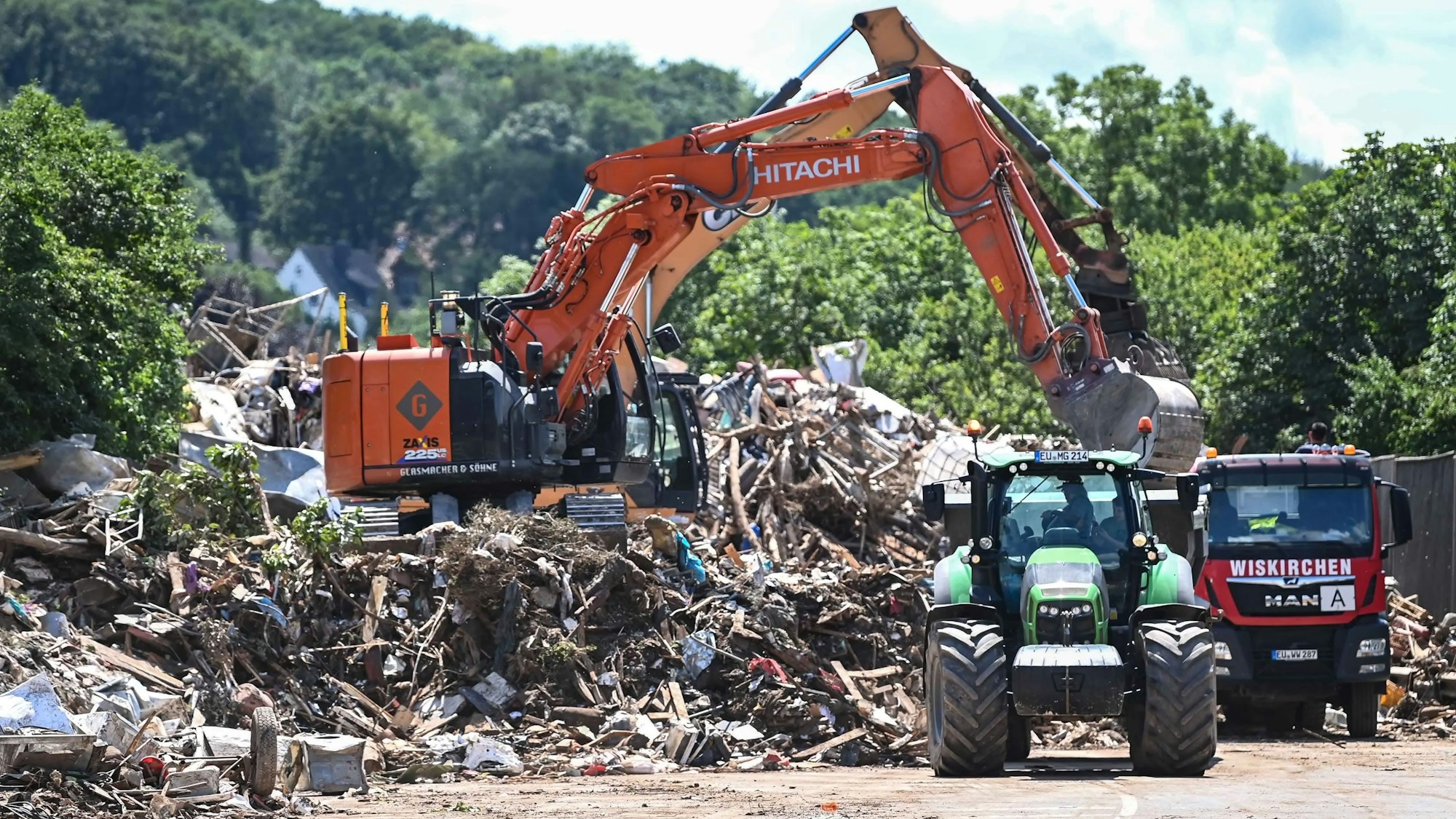 Das Bild zeigt einen Bagger, der Müll auf einen Lkw lädt. Auch ein Traktor samt Anhänger ist zu sehen.