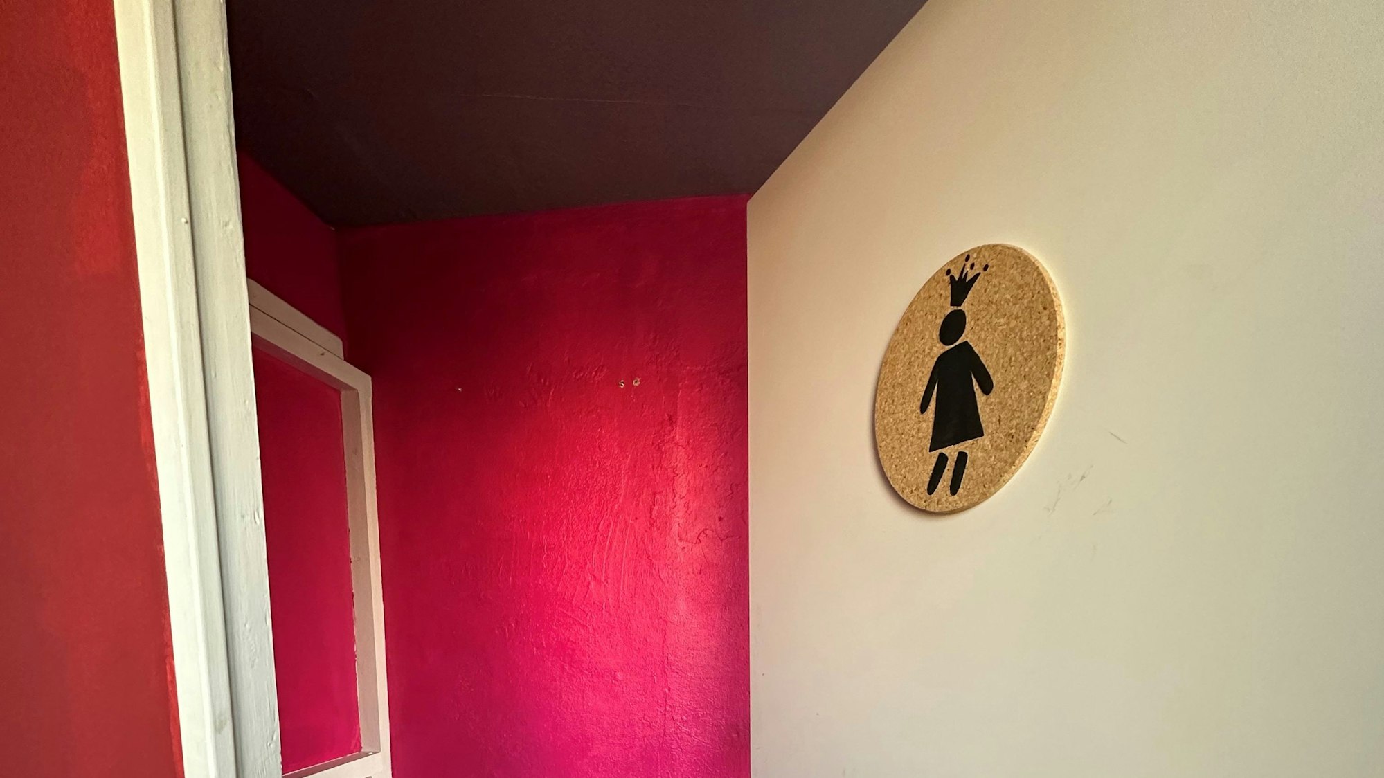 Zu sehen ist die Tür zu einer pink gestrichenen Gästetoilette.