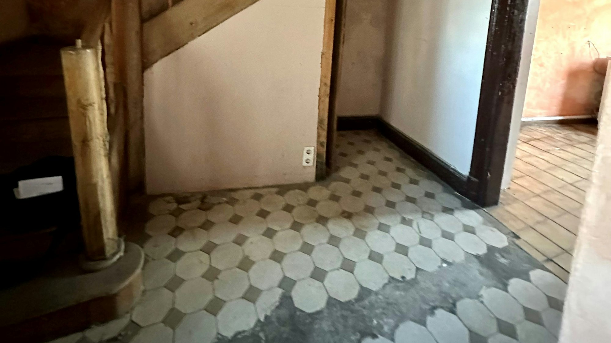 Zu sehen ist ein Treppenhaus aus Holz, auf dem Boden liegen Fliesen.