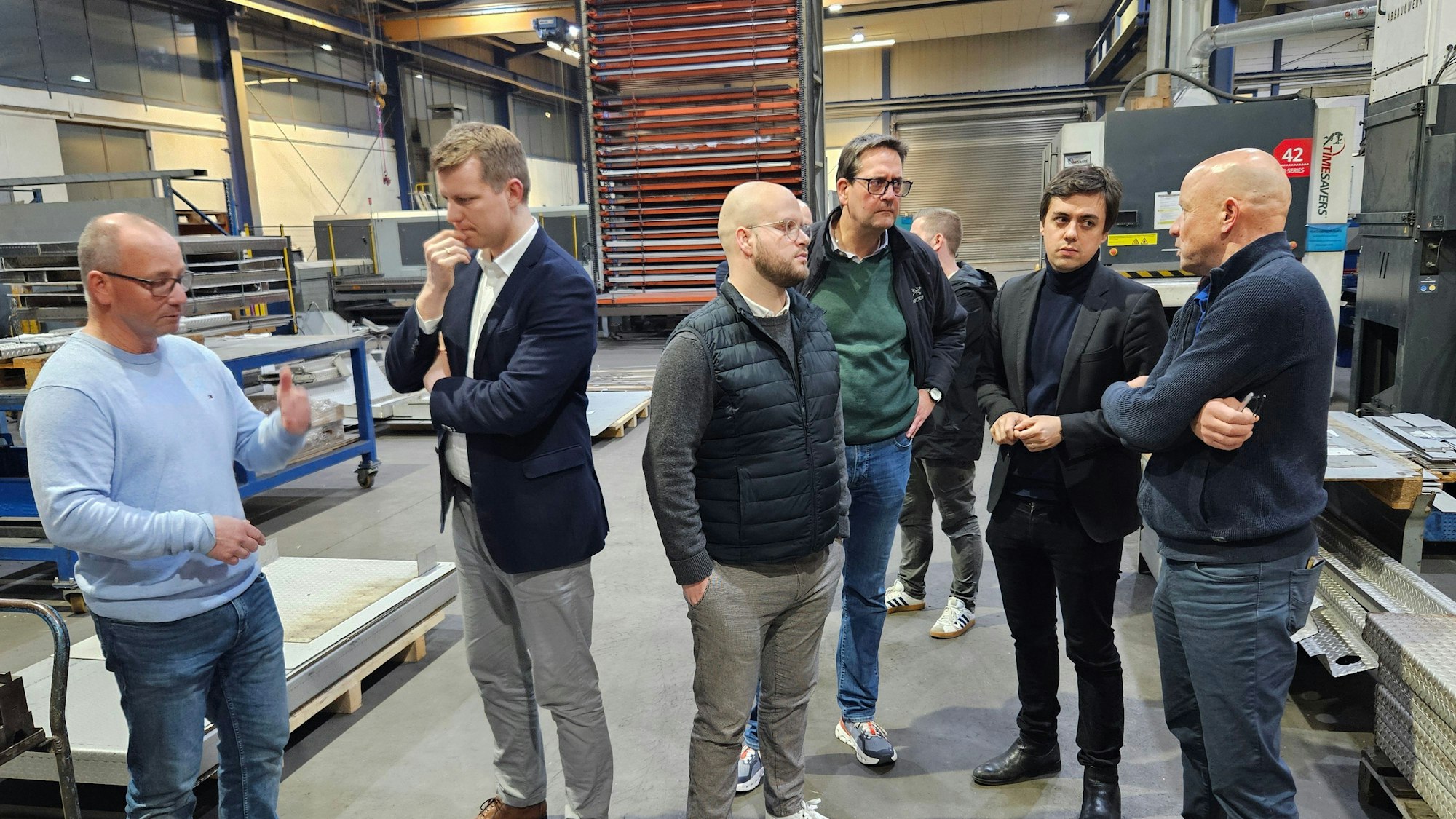 Sechs Männer stehen in einer Werkhalle und sprechen miteinander.