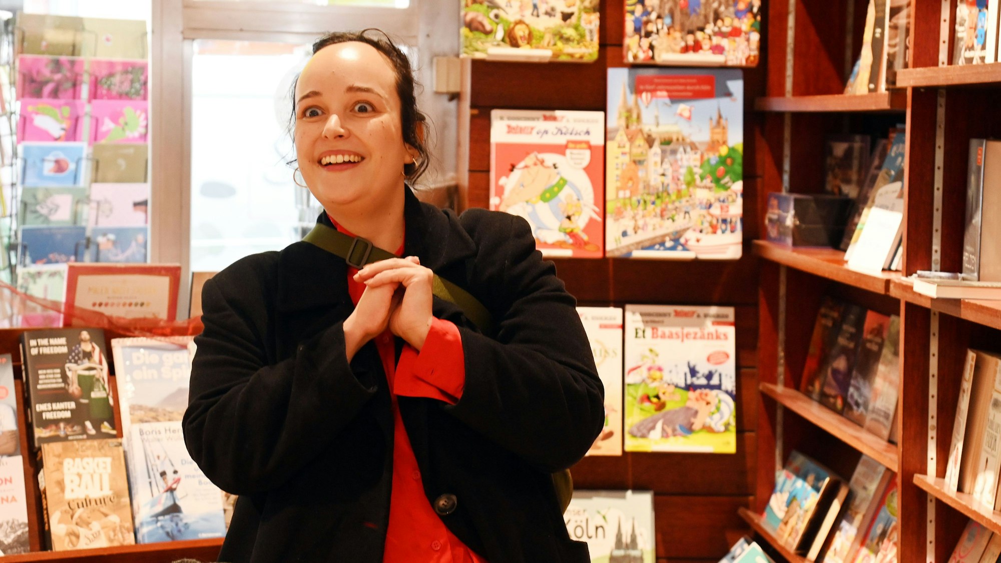 Eine junge Frau steht in einer Buchhandlung inmitten von Regalen.