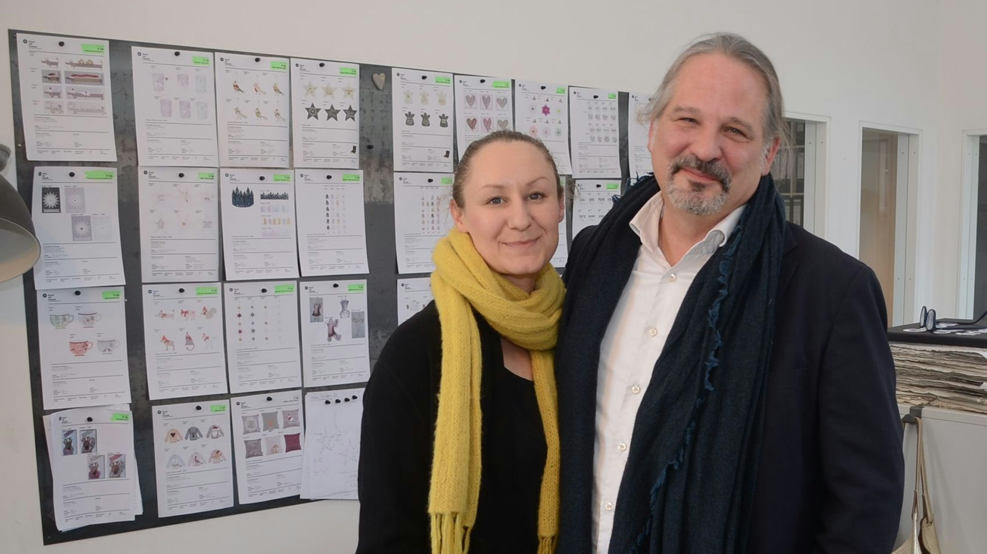 Ein Mann und eine Frau stehen vor einer Wand mit Entwurfszeichnungen.