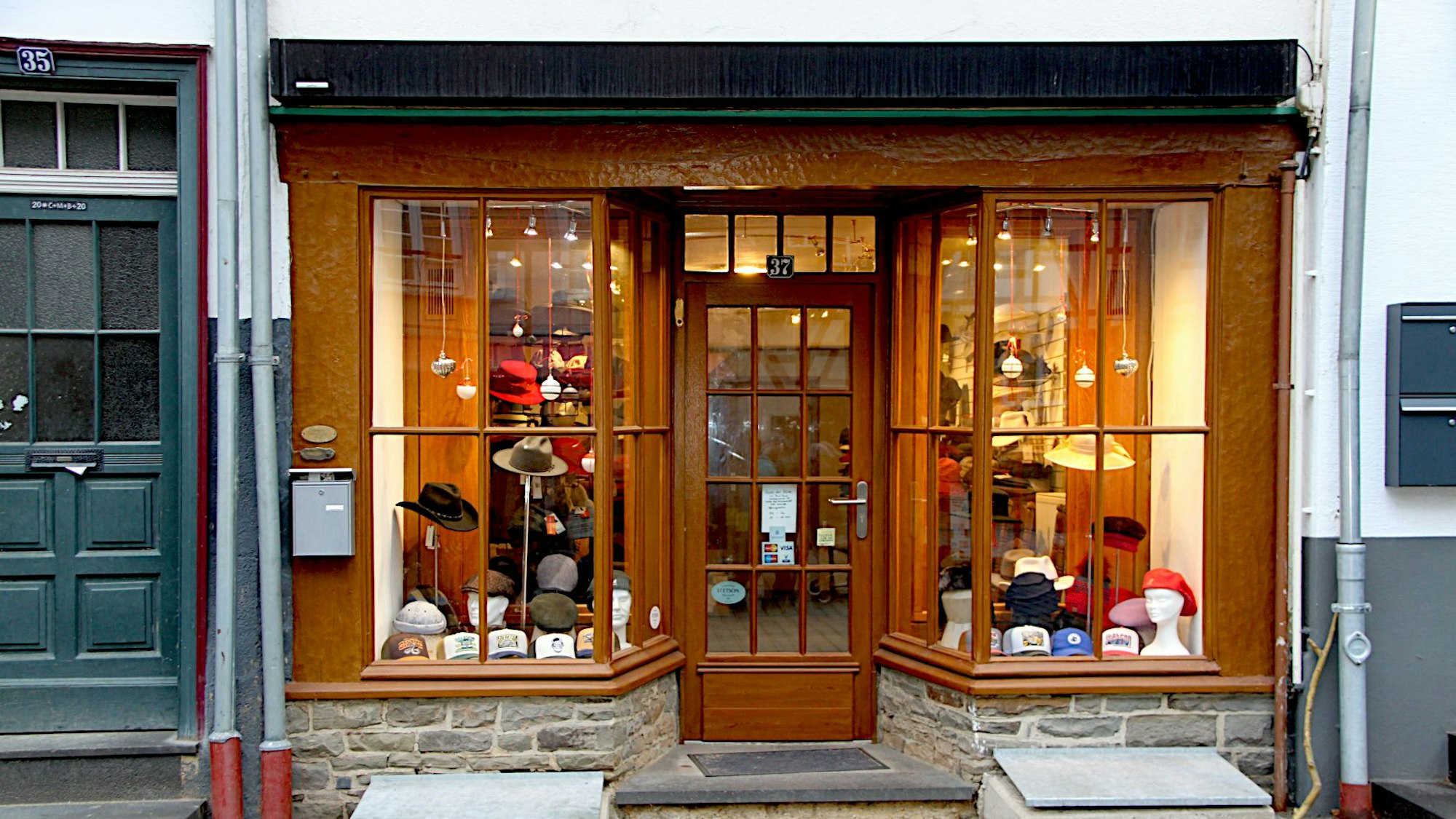 Das Bild zeigt beleuchtete Schaufenster rechts und links einer Tür. Die Rahmen sind aus Holz.