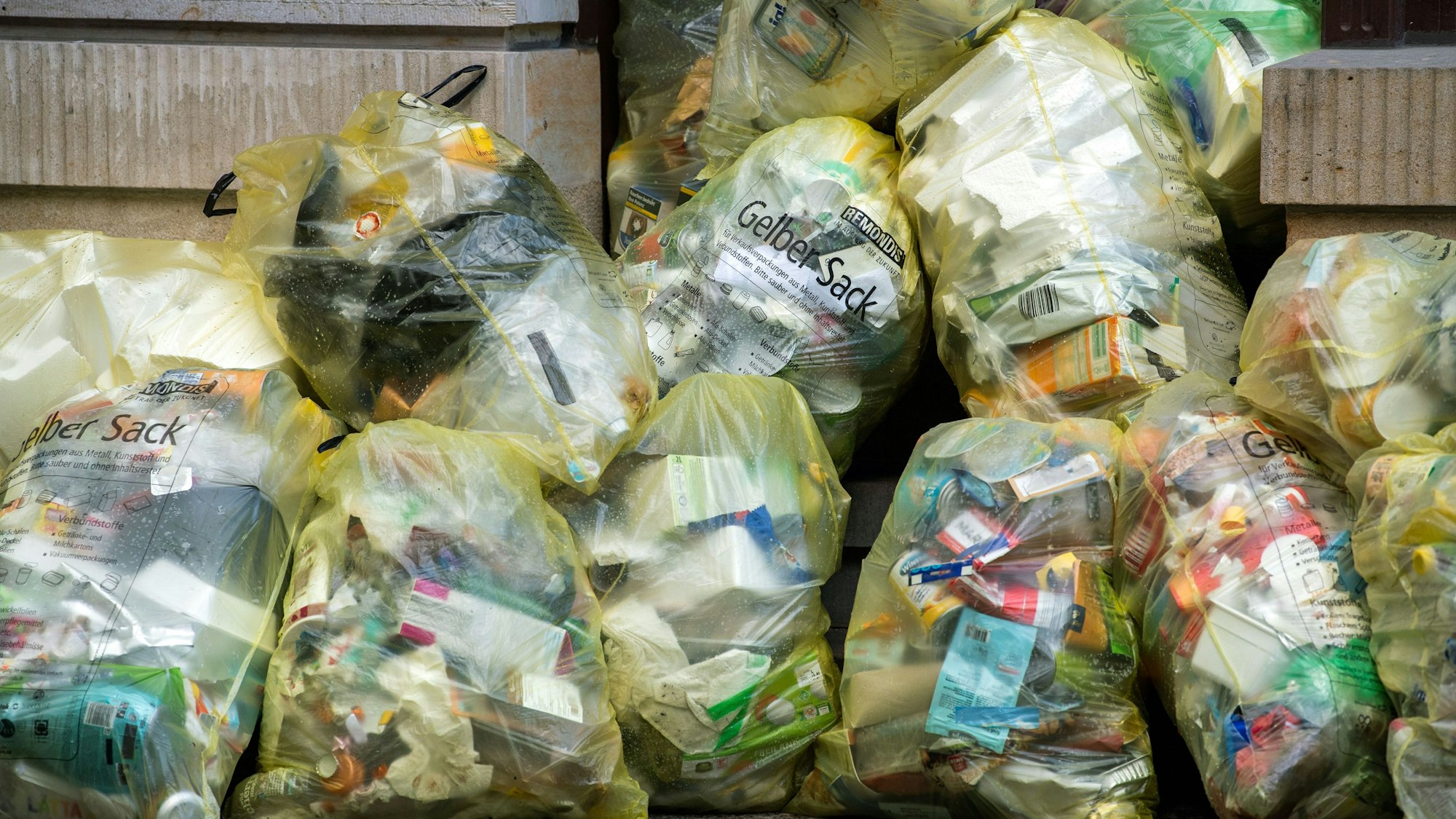 Gefüllte gelbe Abfallsäcke stapeln sich vor einer Wand.