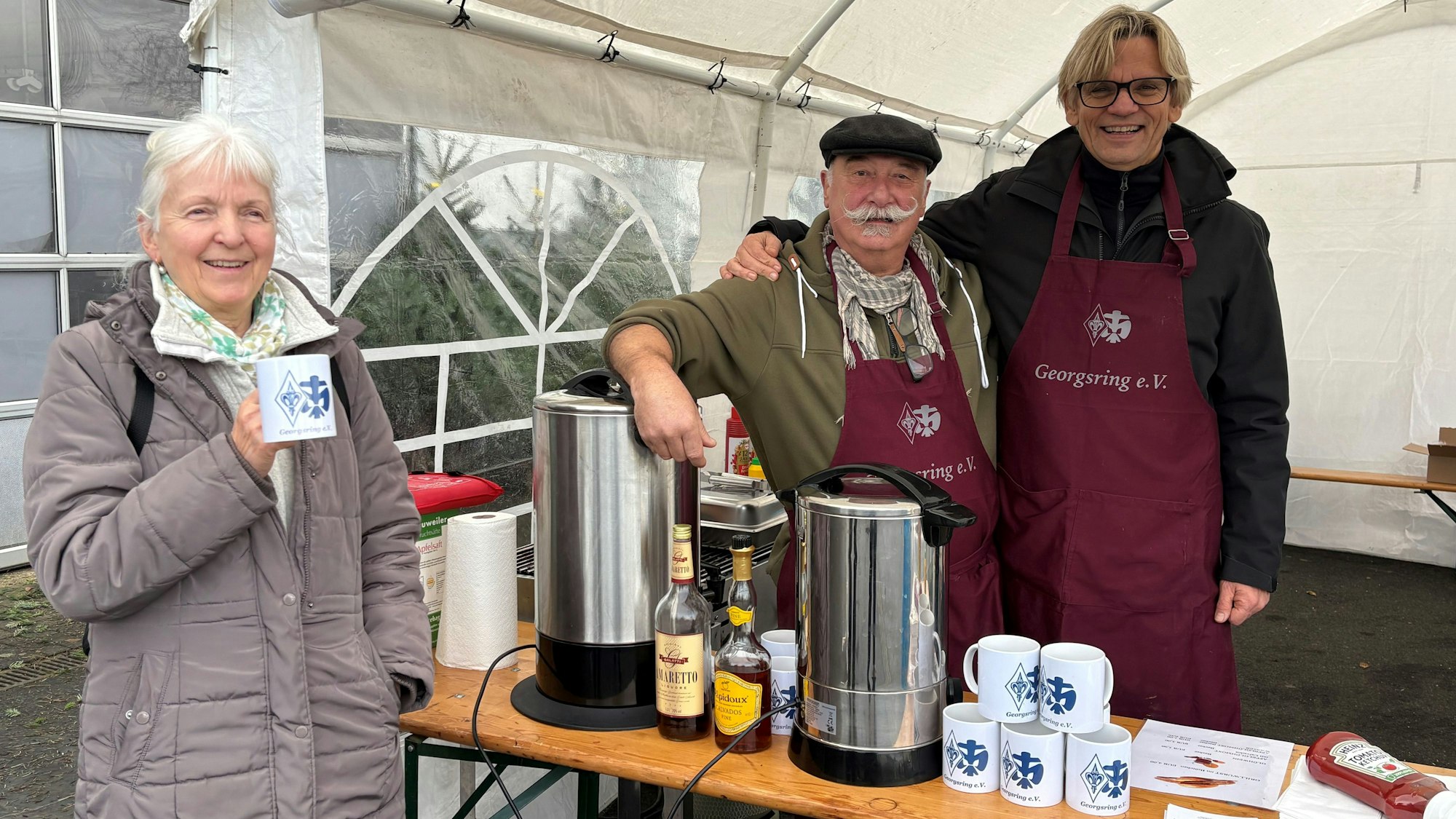 Rheinbacher Pfadfinder verkaufen Weihnachtsbäume. Eine Kundin trinkt Glühwein bei Wolfgang Bures (l.) und Günter Rödel. Auch Bratwürstchen gibt es bei den beiden.