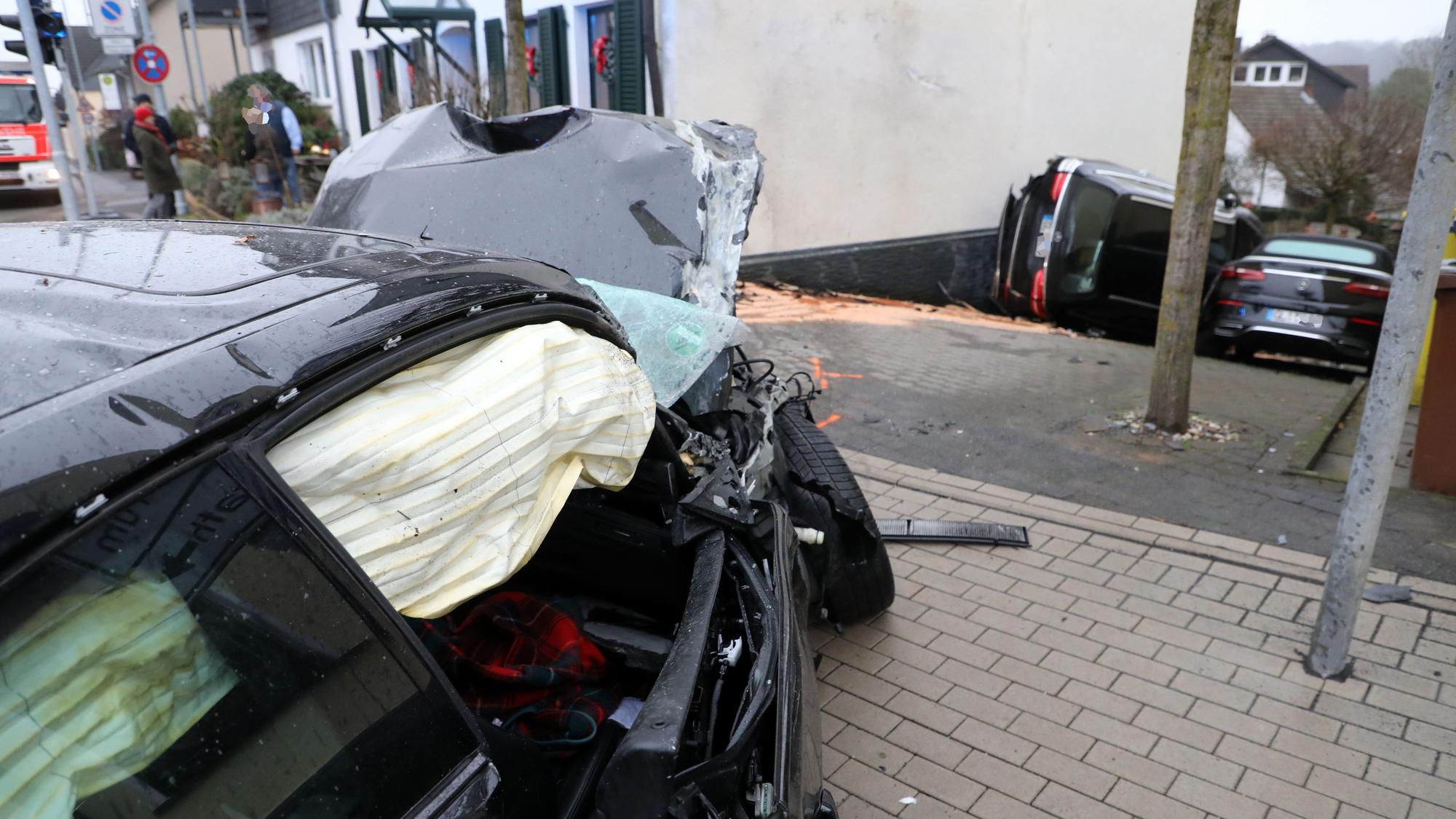 Ein Unfallwagen steht mit ausgelösten Airbags einige Meter von einem haus entfernt. hat die Feuerwehr schon von der Hausecke, in die er gekracht ist, zurückgezogen. Die beiden Fahrzeuge im Hintergrund hat der Wagen die Einfahrt hinuntergderückt.