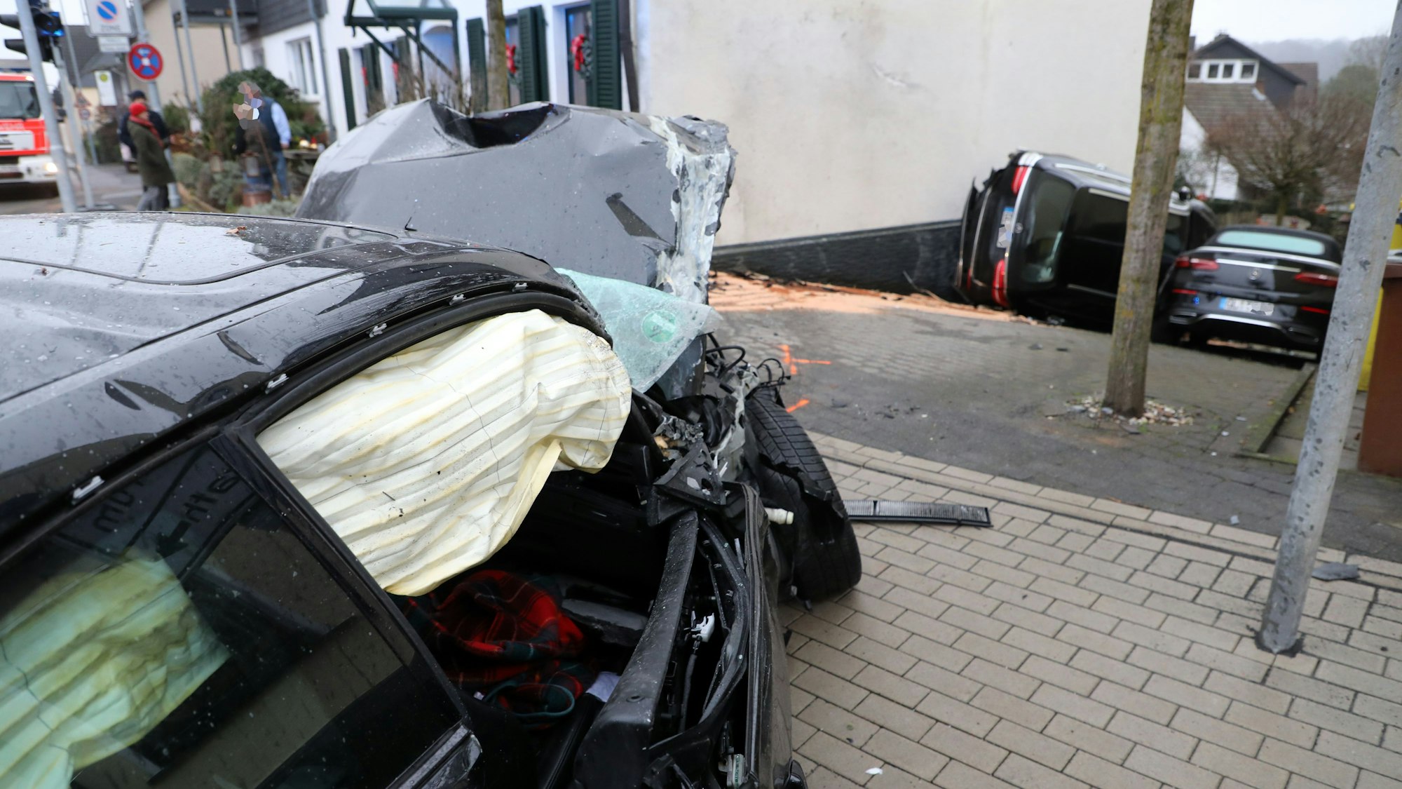 Ein Unfallwagen steht mit ausgelösten Airbags einige Meter von einem haus entfernt. hat die Feuerwehr schon von der Hausecke, in die er gekracht ist, zurückgezogen. Die beiden Fahrzeuge im Hintergrund hat der Wagen die Einfahrt hinuntergderückt.