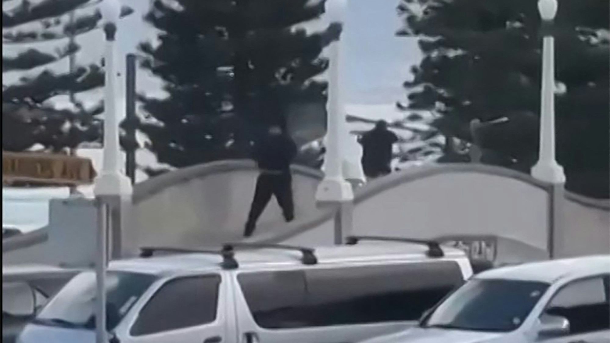 TOPSHOT - This screen grab made from UGC handout video footage courtesy of Timothy Brant-Coles shows two gunmen dressed in black firing multiple shots on a bridge at Bondi Beach in Sydney on December 14, 2025. Australian police said two people were in custody following reports of multiple gunshots on December 14 at Sydney's famed Bondi Beach, urging the public to take shelter. (Photo by Handout / various sources / AFP) / RESTRICTED TO EDITORIAL USE - MANDATORY CREDIT "AFP PHOTO / COURTESY OF TIMOTHY BRANT-COLES" - HANDOUT - NO MARKETING NO ADVERTISING CAMPAIGNS - DISTRIBUTED AS A SERVICE TO CLIENTS - NO ARCHIVE