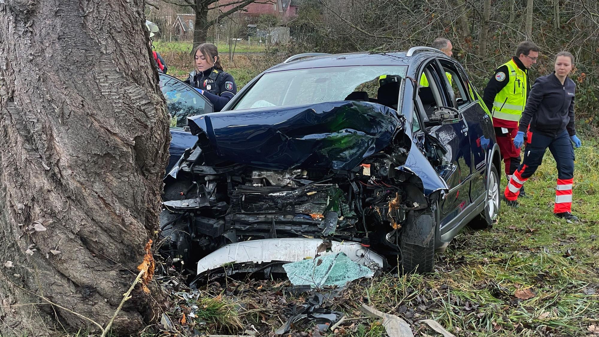 Polizeibeamte und Helfer des Rettungsdienstes an der Unfallstelle hinter dem im Frontbereich total zerstörten Fahrzeug.