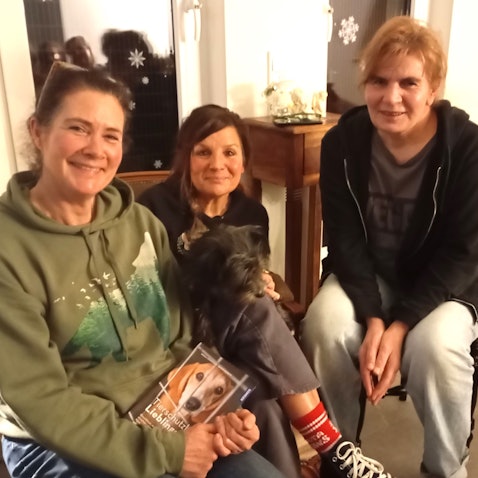 Das Foto zeigt die drei Frauen, eine mit einem Hund auf dem Schoß.
