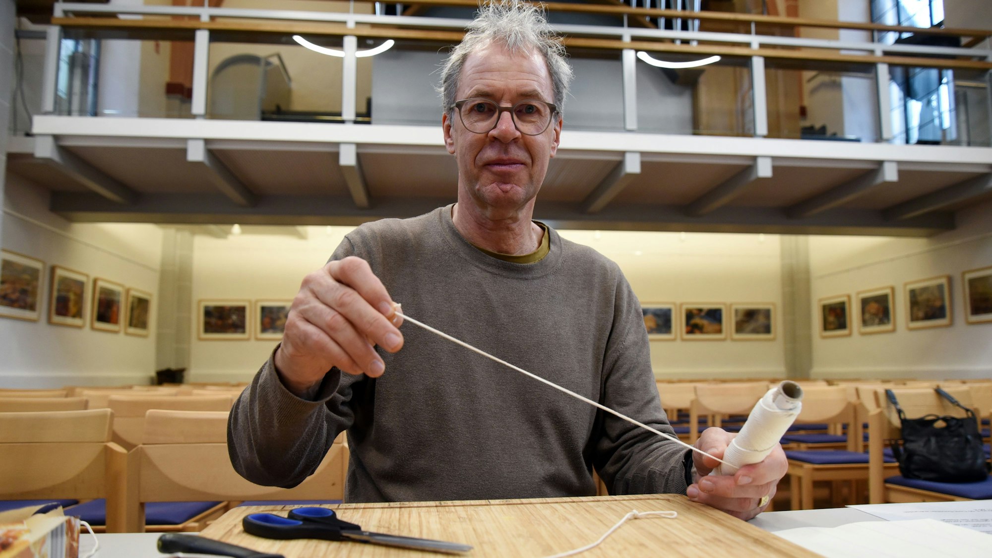 Ein Mann sitzt mit einer Rolle voll Kerzendocht in der Hand an einem Tisch.