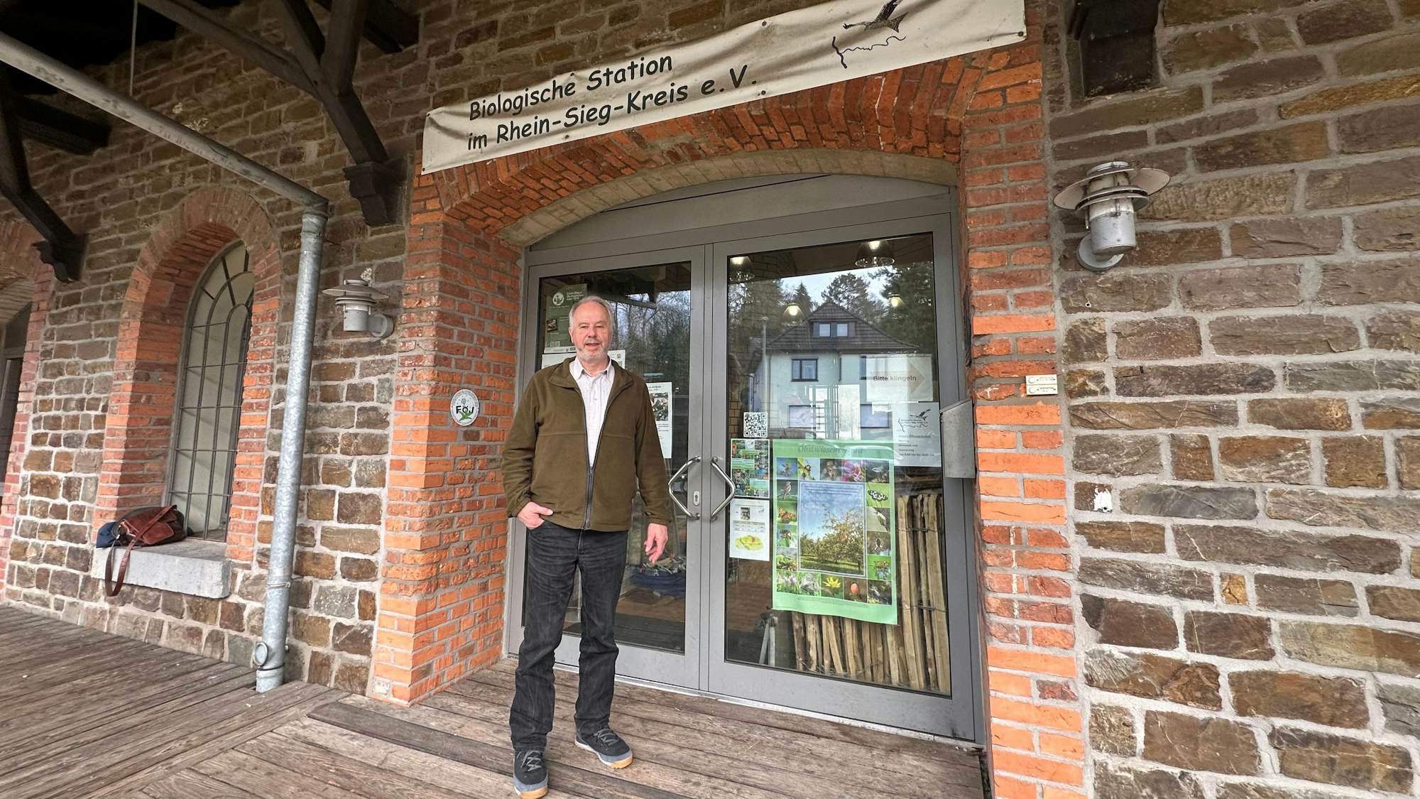 Dr. Dieter Steinwarz vor der Eingangstür zur Biologischen Station des Rhein-Sieg-Kreises in Eitorf. Auf dem Logo ist rechts der Rotmilan zu erkennen, das Wappentier der Station.