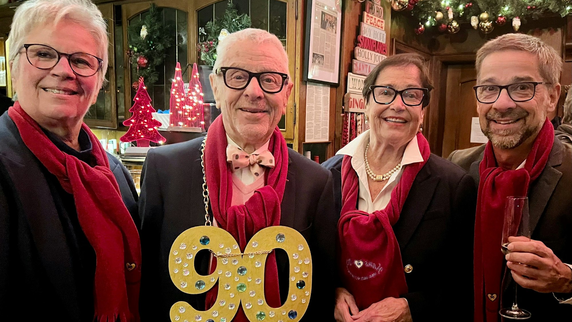 Ein Mann mit einer goldenen 90 um den Hals steht in einer Kneipe, neben ihm seine Frau und seine erwachsenen Kinder.