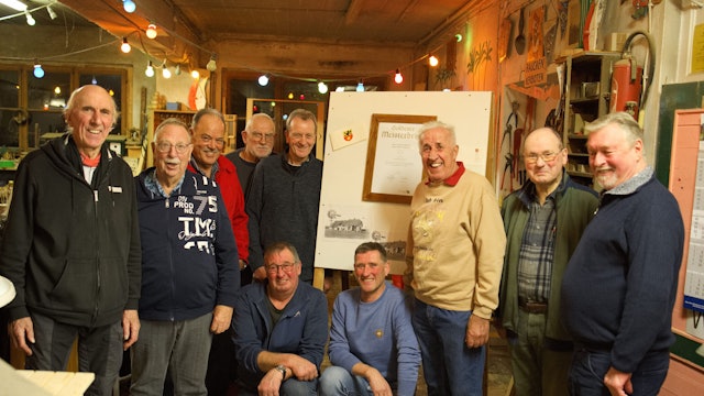 Schreiner Hans-Peter Lückerath steht vor dem gerahmten goldenen Meisterbrief. Er ist umringt von ehemaligen Gesellen.