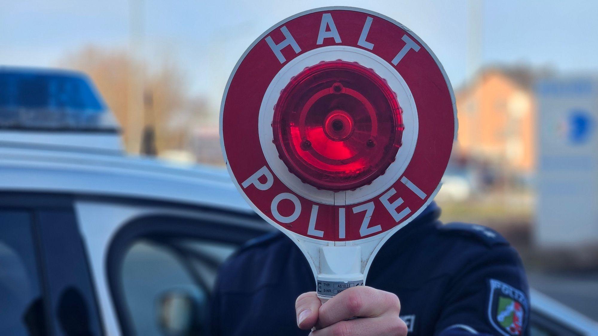 Zu sehen ist ein Polizist, der eine Kelle hält.