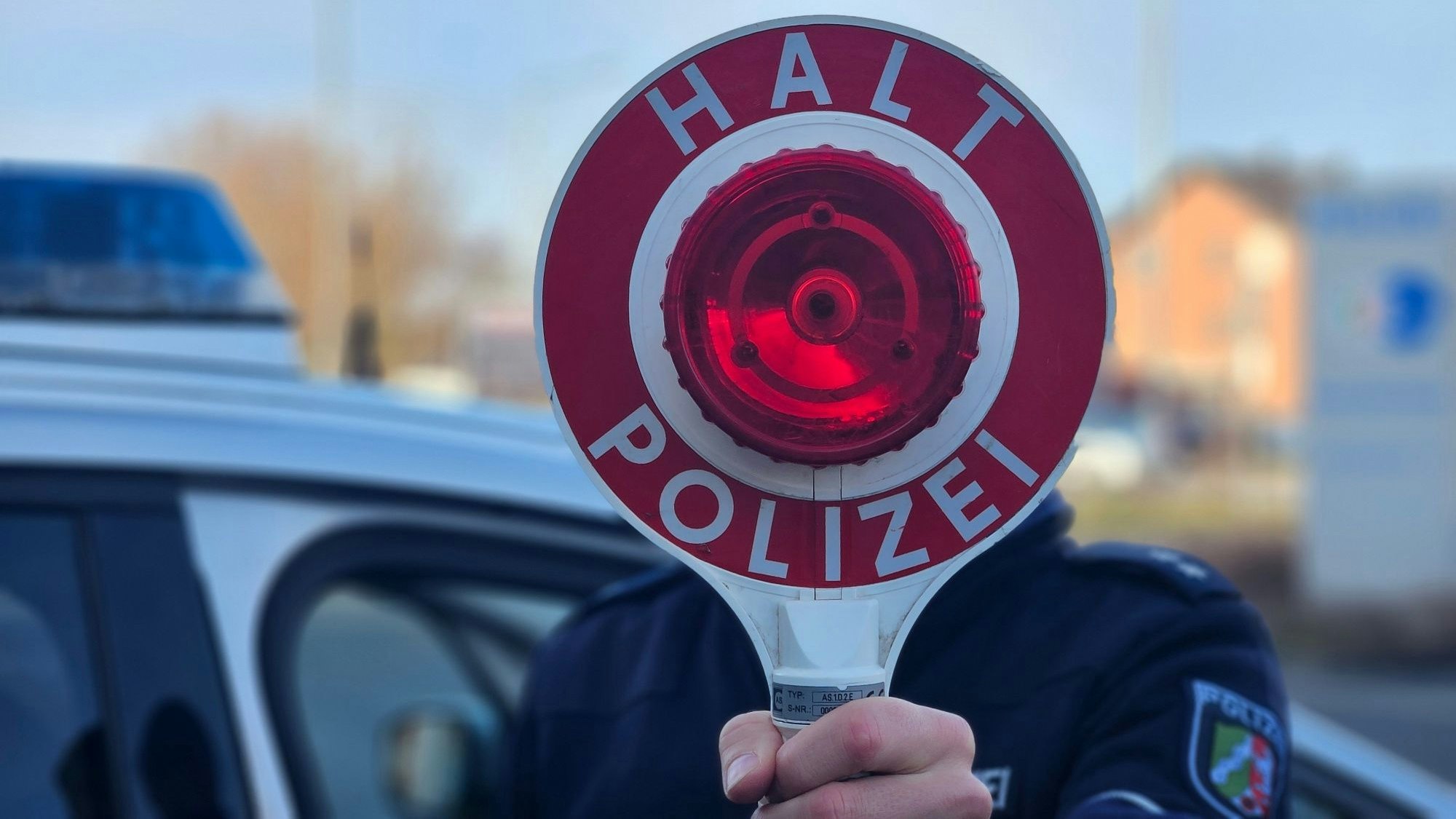 Zu sehen ist ein Polizist, der eine Kelle hält.